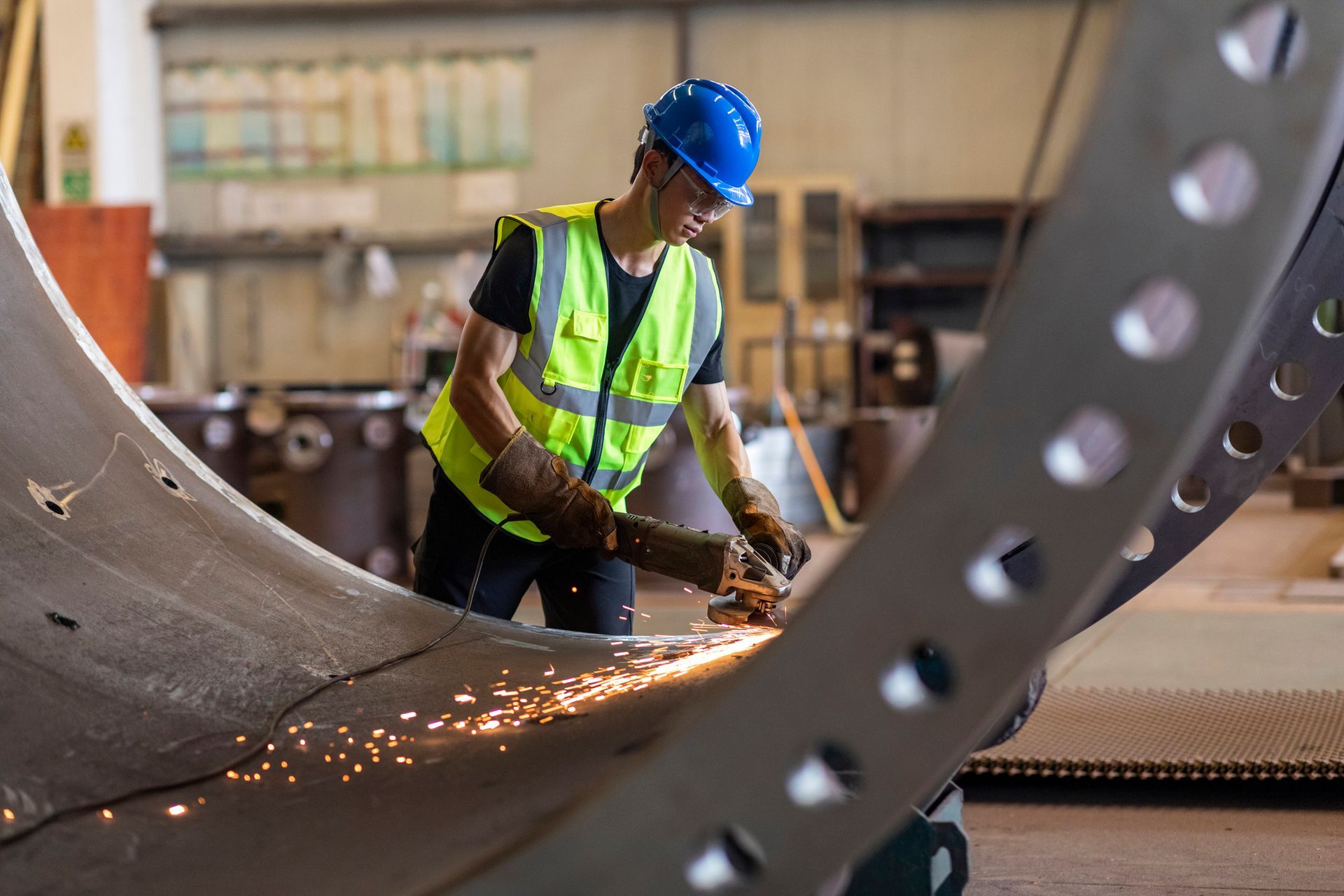 Worker in safety gear grinding metal during steel fabrication in industrial workshop. Worker in safety gear grinding metal during steel fabrication in industrial workshop.