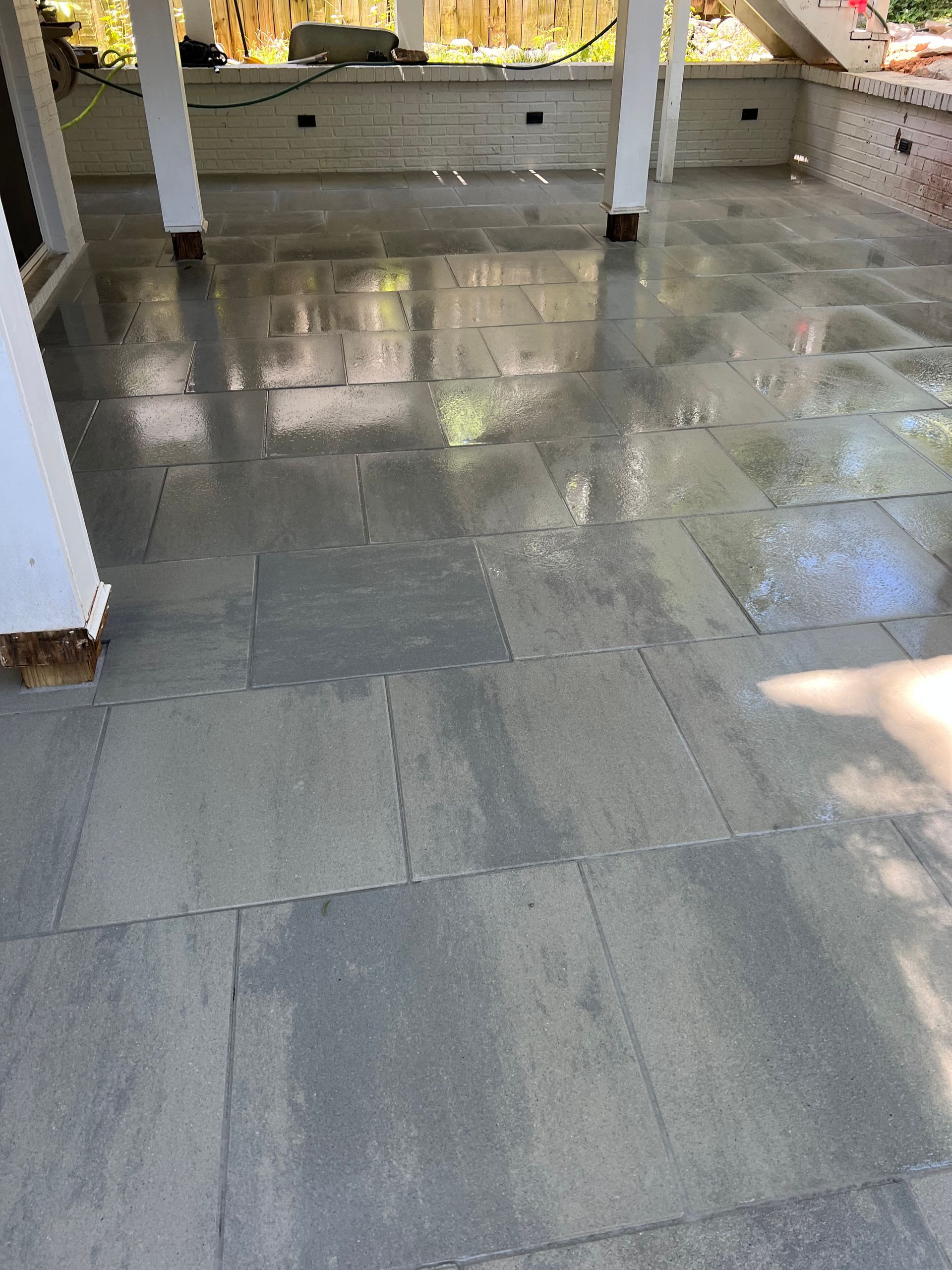 A patio with a lot of tiles on it and a pool in the background.