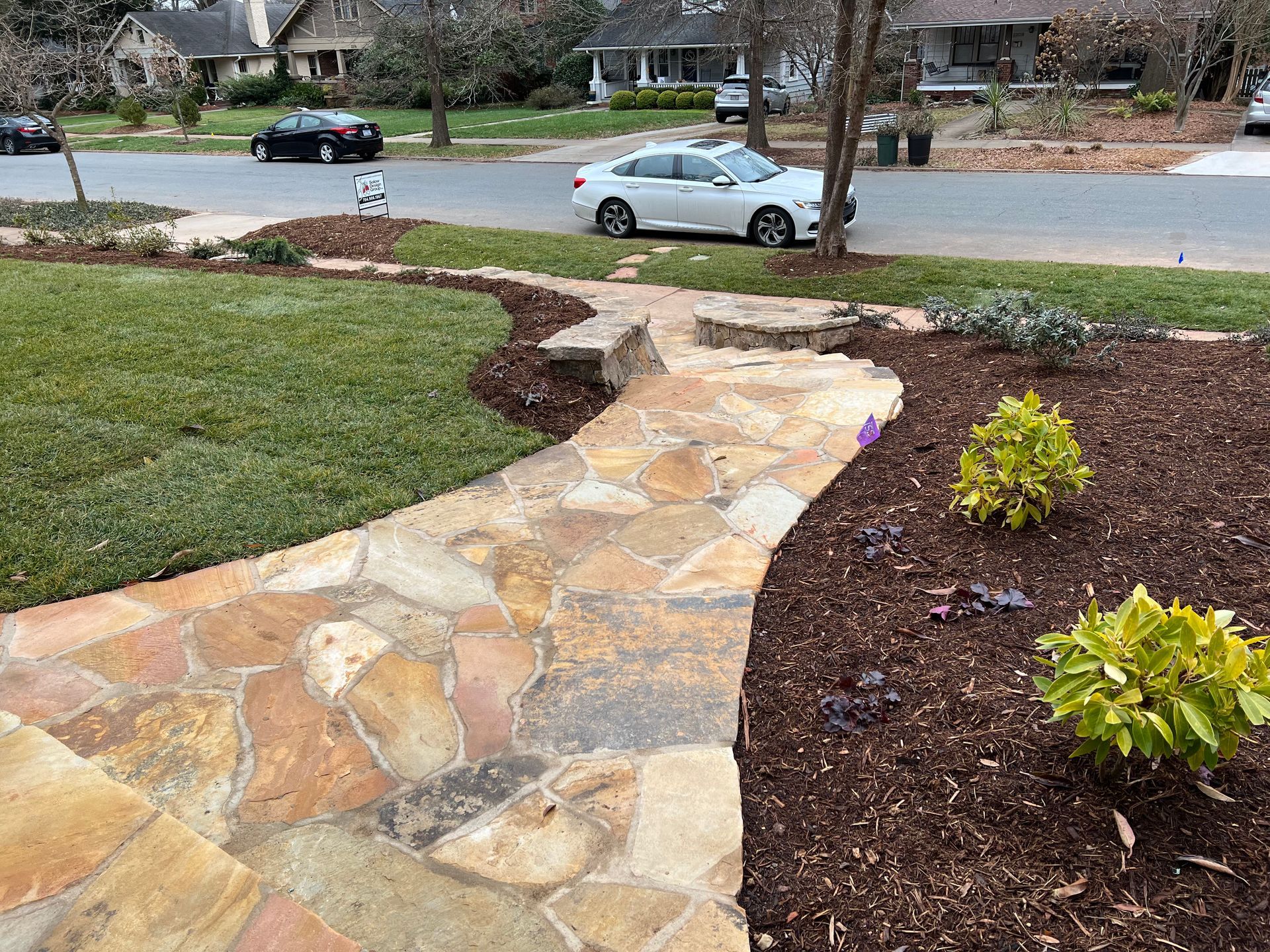 A white car is parked on the side of the road next to a stone walkway.