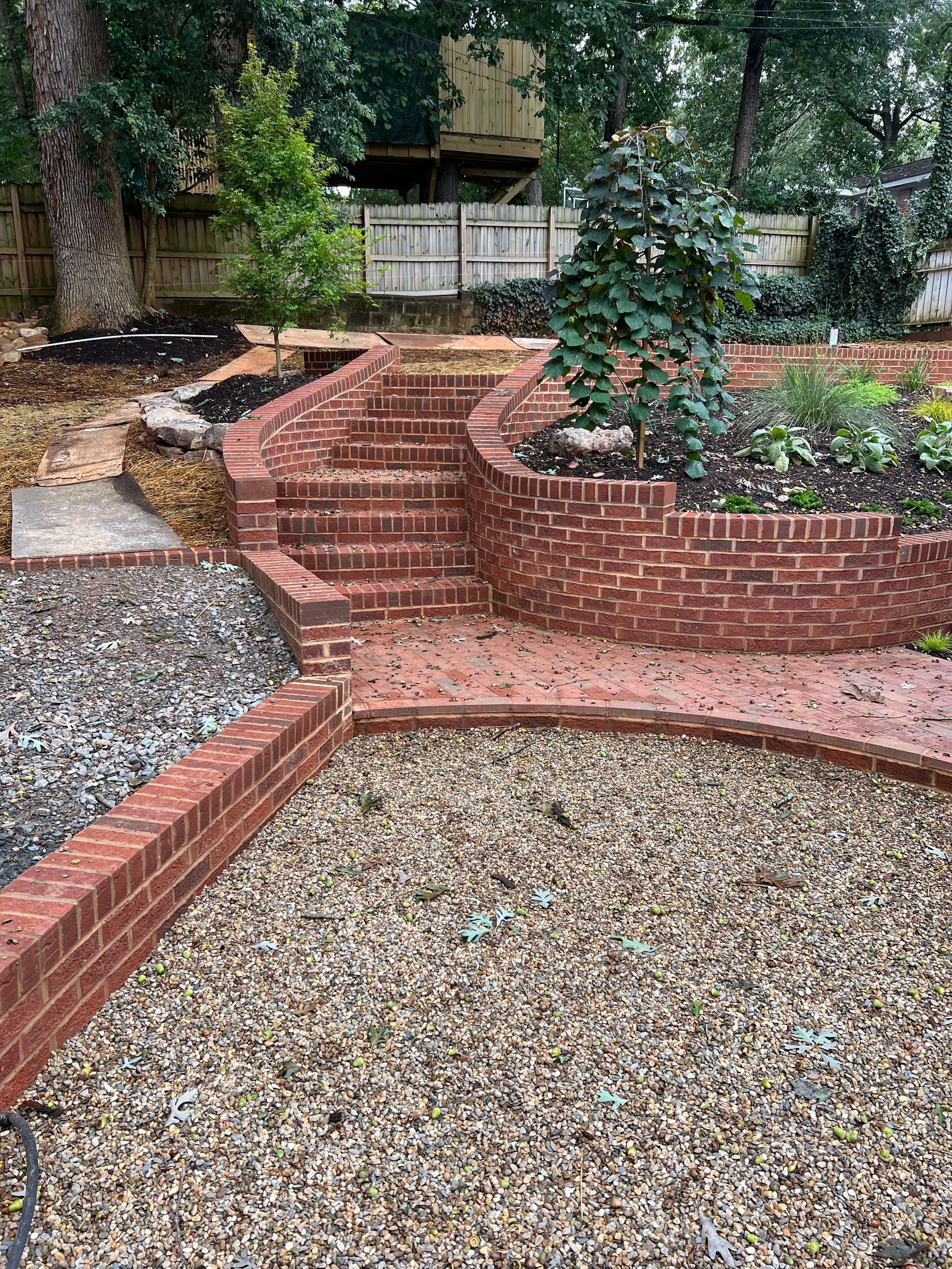 A brick walkway with stairs leading up to a gravel area in a backyard.