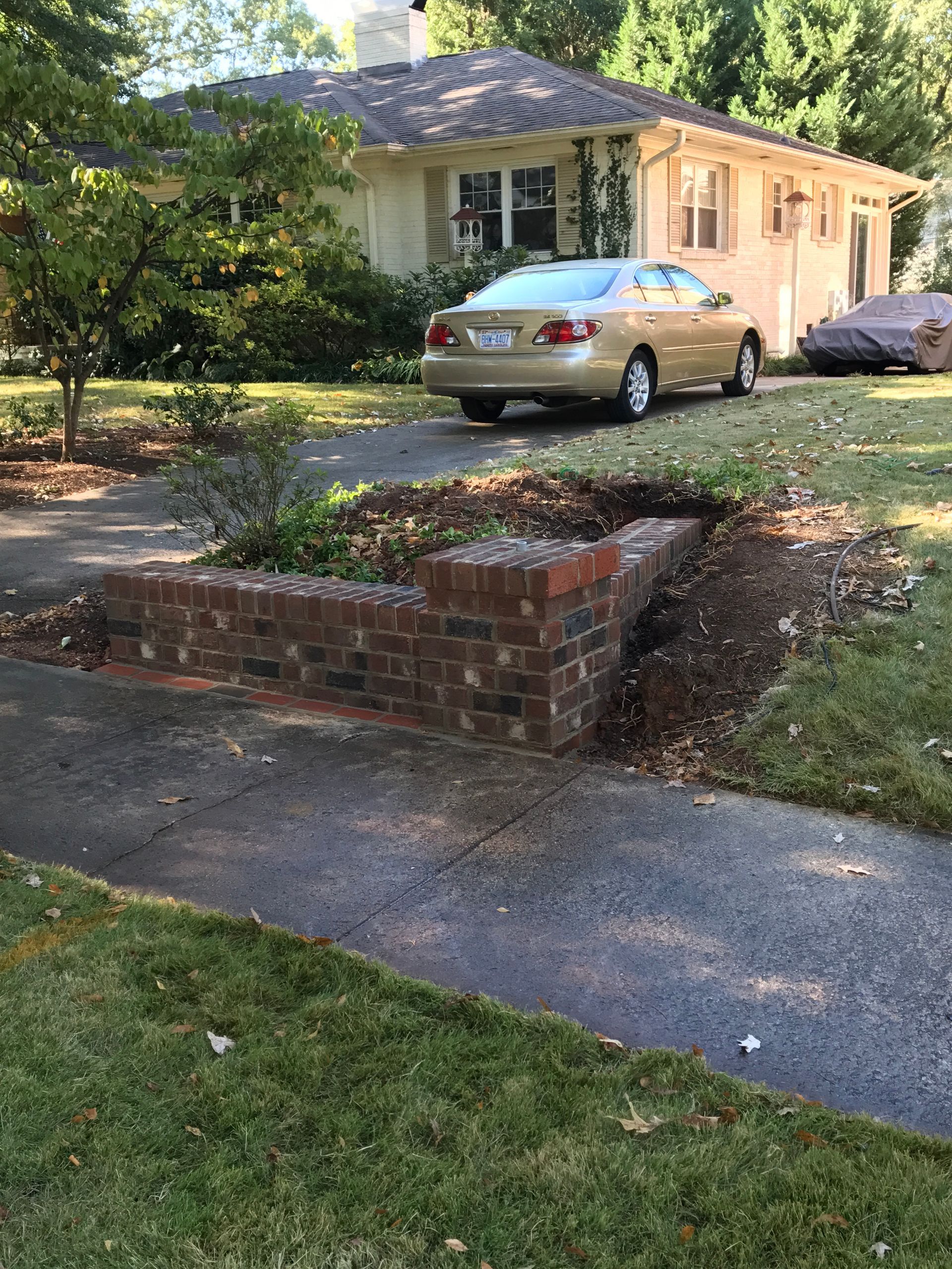 A car is parked in front of a house next to a brick wall.