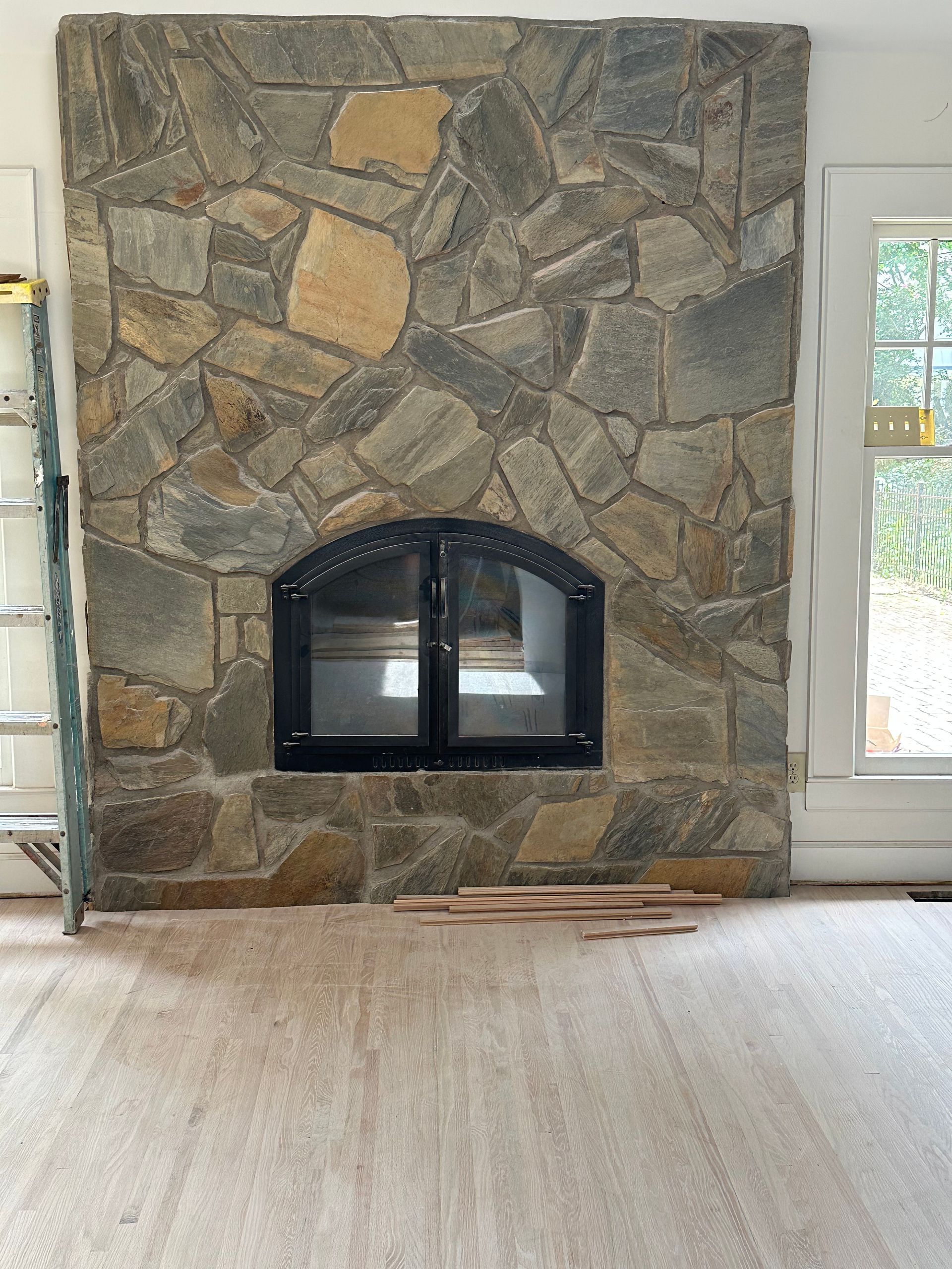 An empty room with a stone fireplace and a ladder