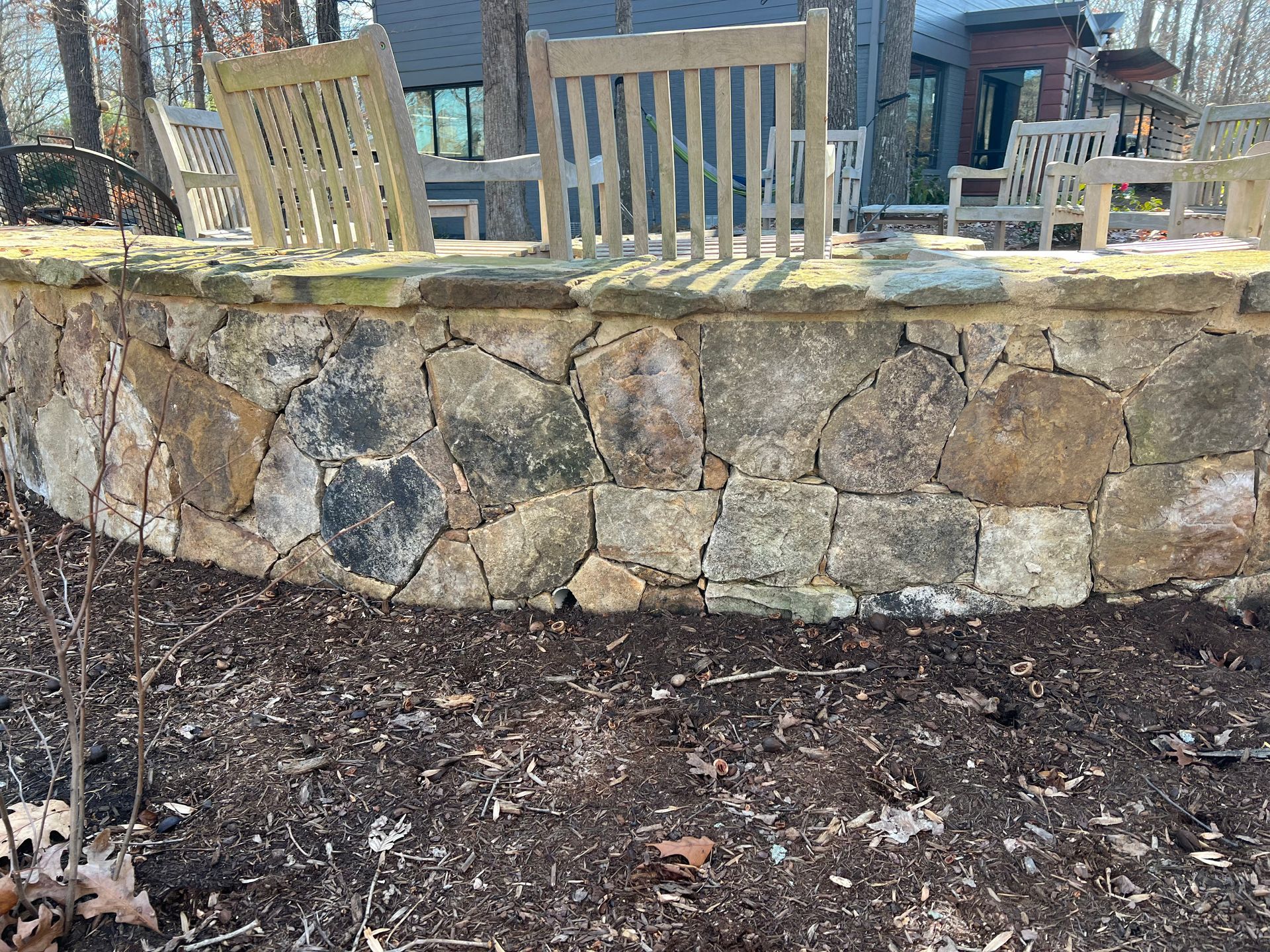 Two wooden chairs are sitting on top of a stone wall.