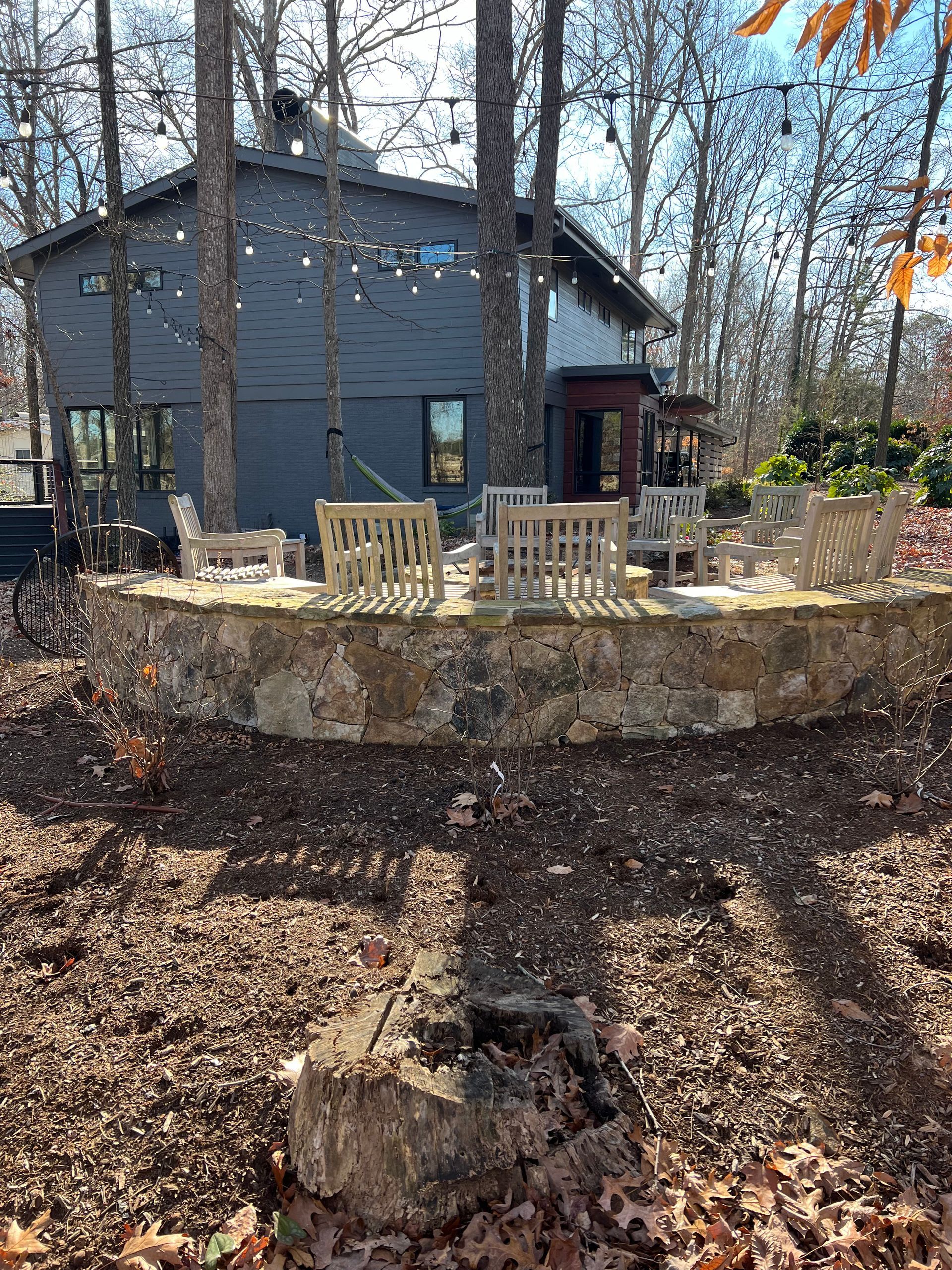 A house with a stone wall and chairs in front of it in the woods.