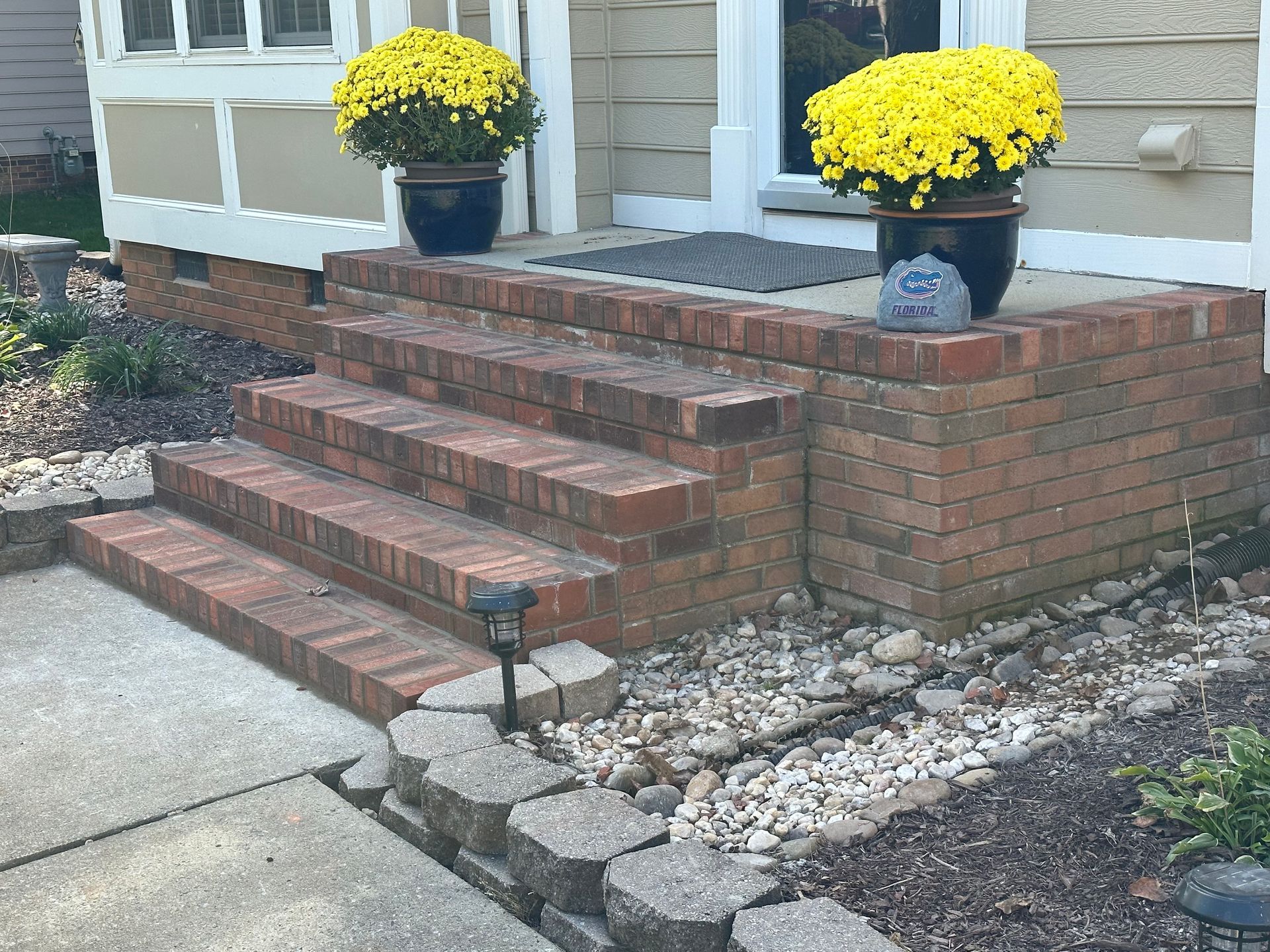 A brick porch with yellow flowers in pots on it