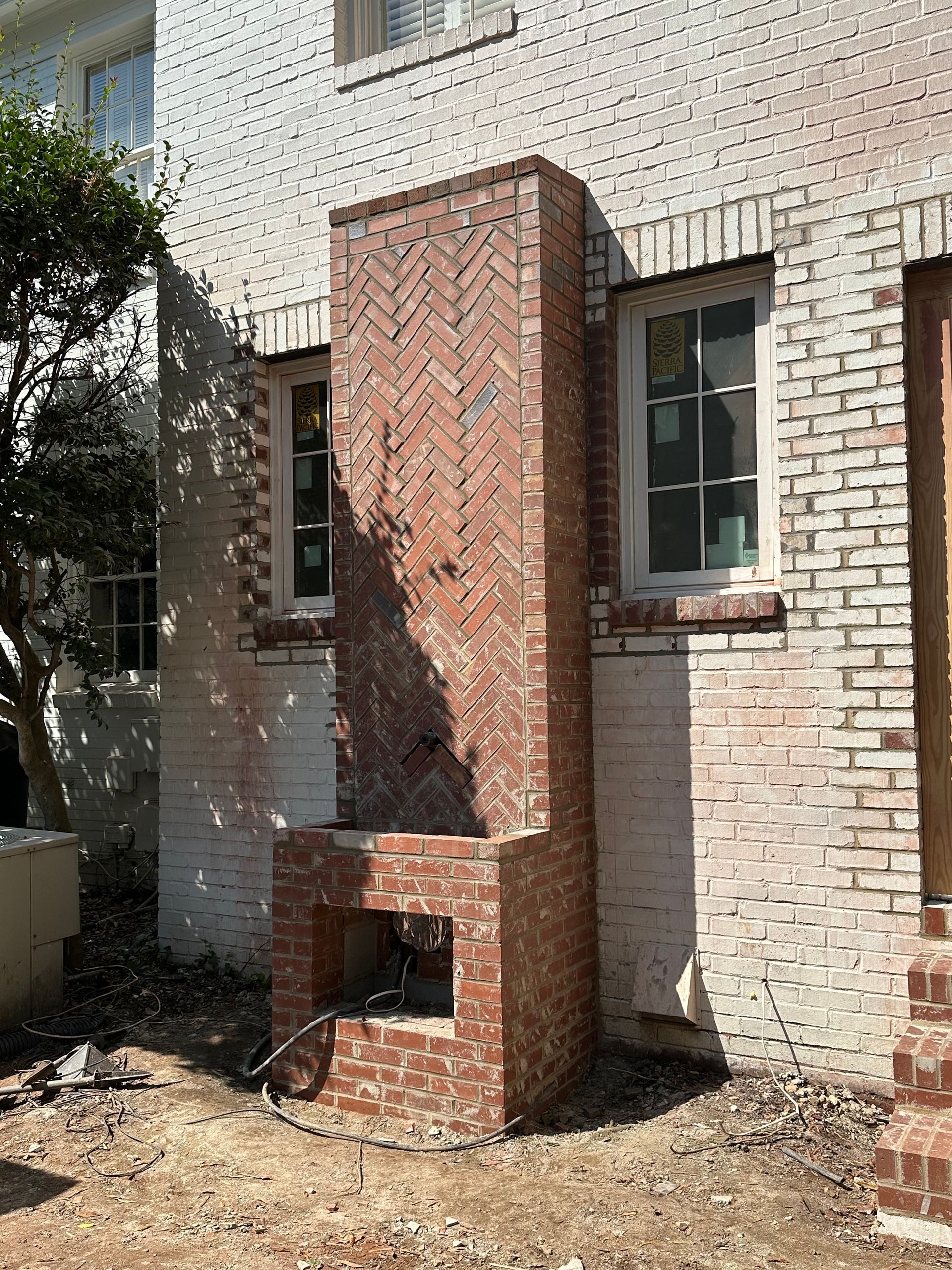 A brick fireplace is being built on the side of a white brick house.