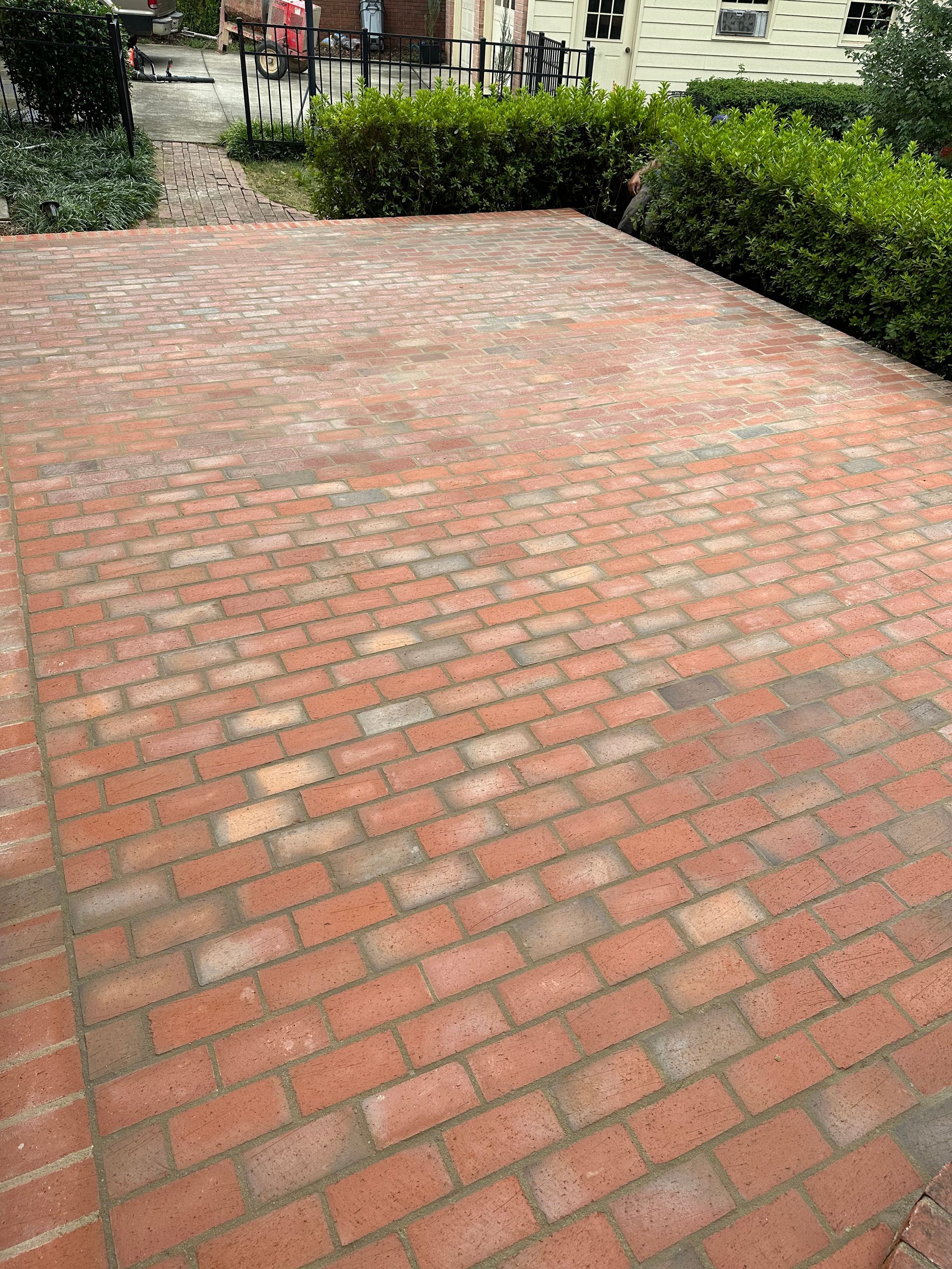 A brick driveway with a fence and bushes in the background.