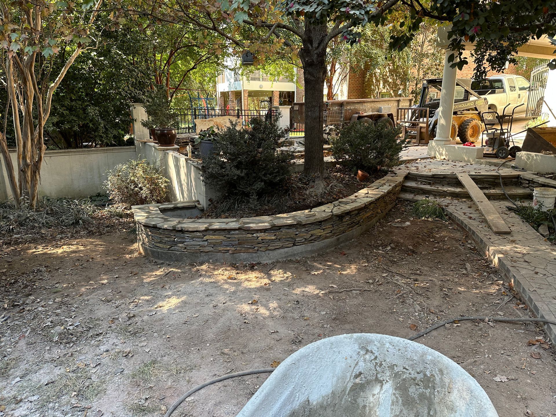 A concrete planter is sitting in the middle of a dirt yard.