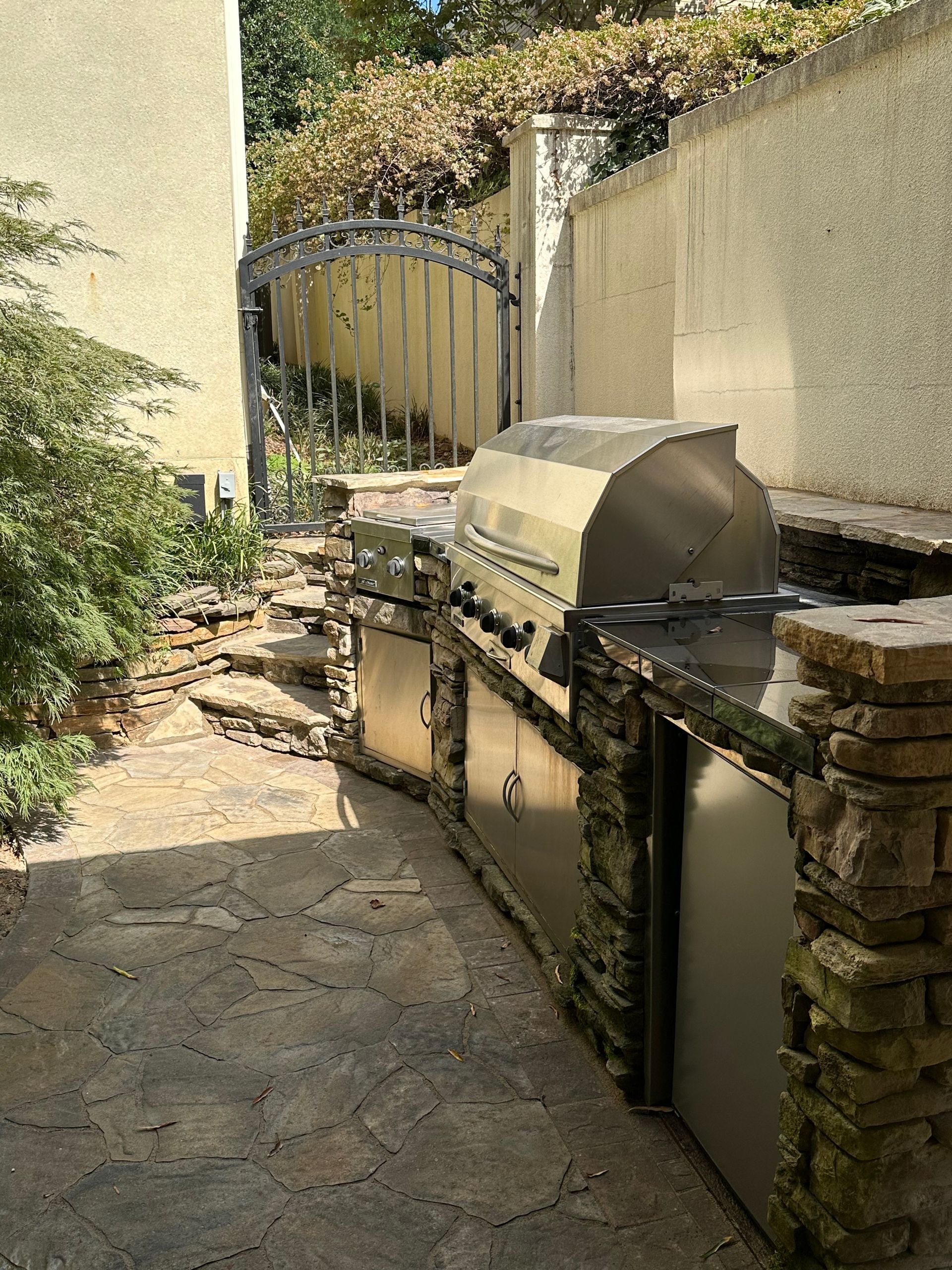 A stainless steel grill is sitting on a patio next to a stone wall.