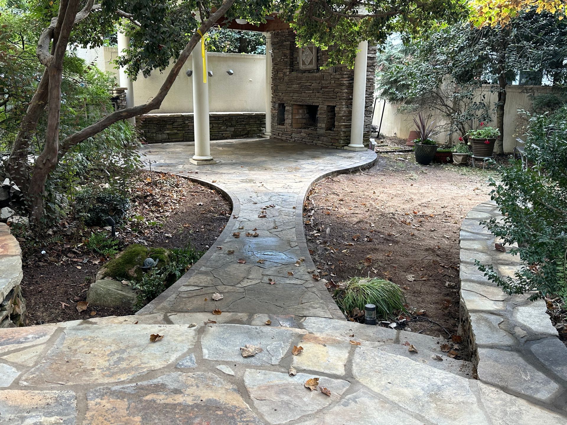 There is a stone walkway leading to a fireplace in the backyard.