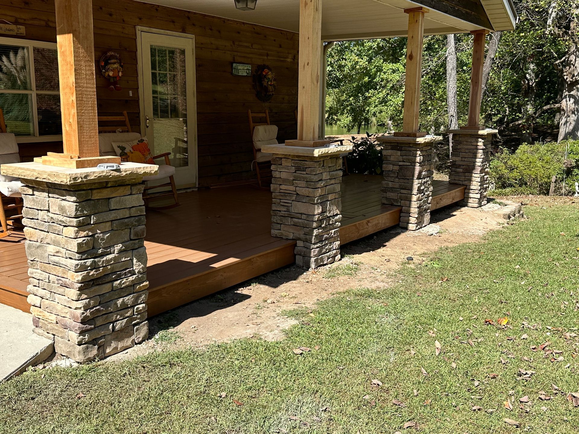A porch with stone pillars and a wooden deck.