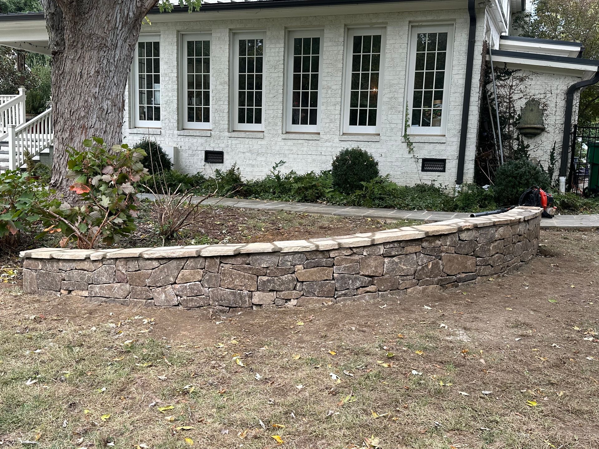 There is a stone wall in front of a white house.