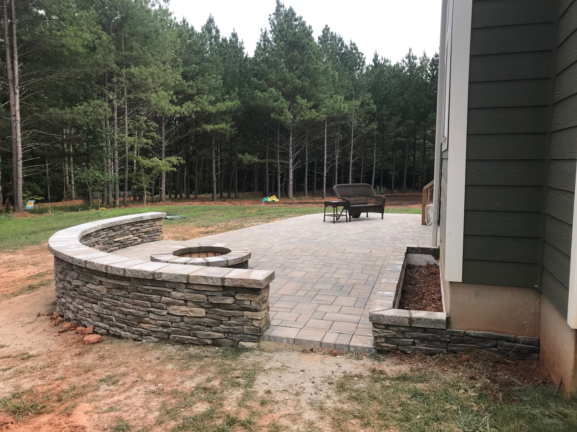 A patio with a fire pit and a stone wall next to a house.