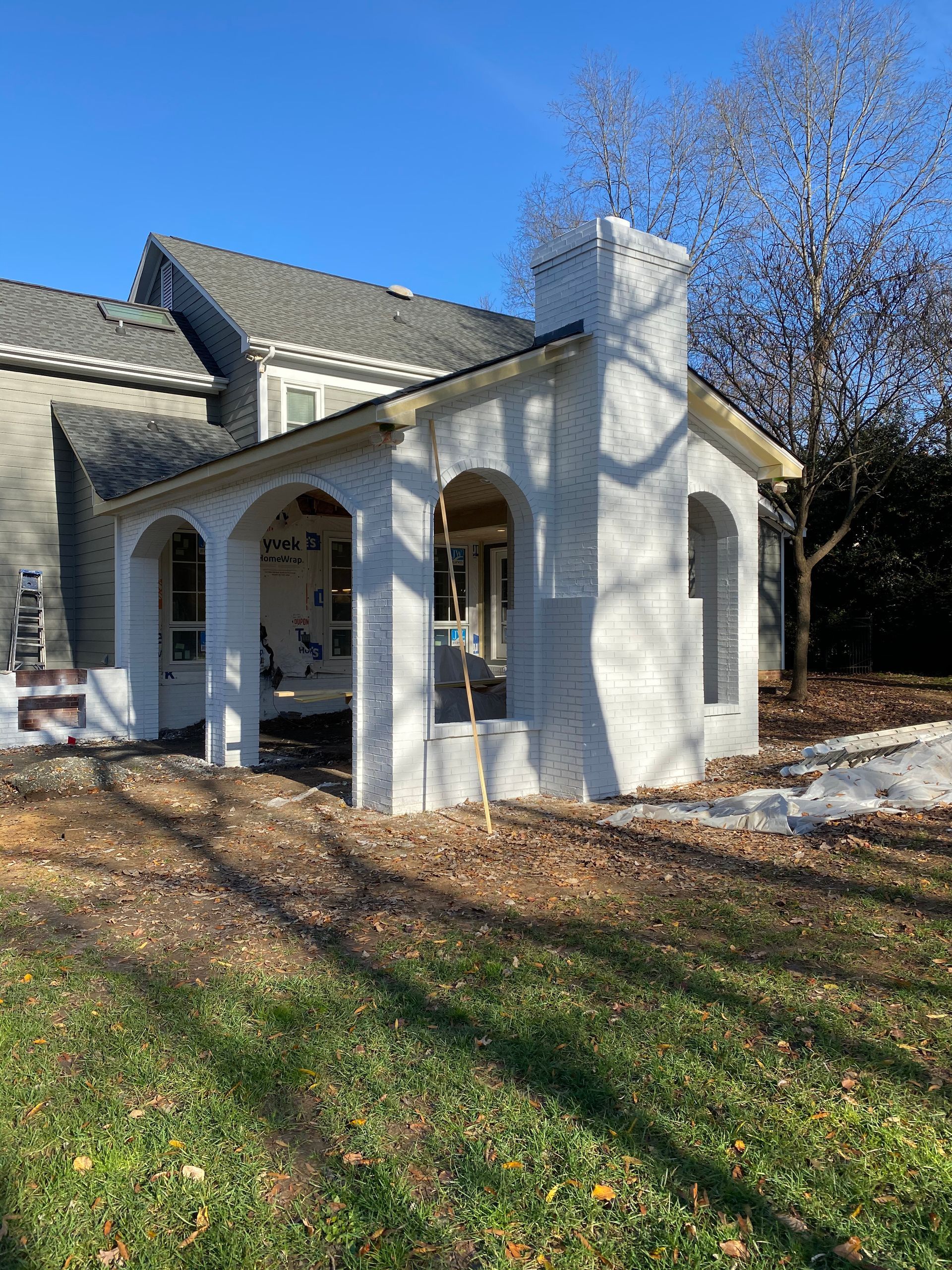 A white house with a porch and a chimney in the backyard.