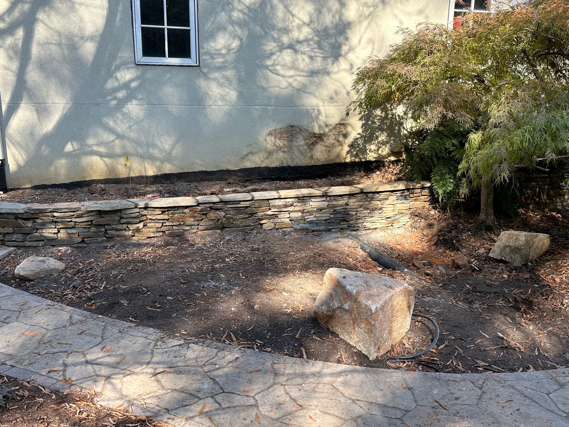 A stone walkway leading to a house with a stone wall in front of it.