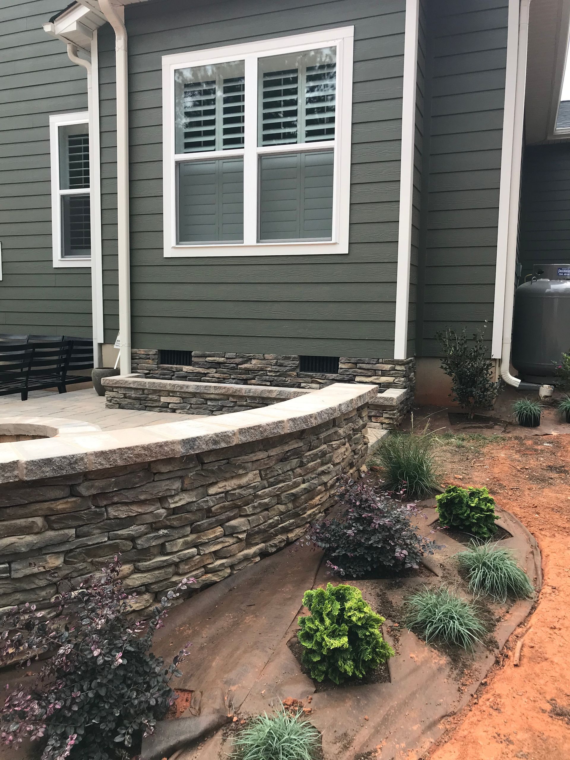 A house with a stone wall and a patio in front of it.