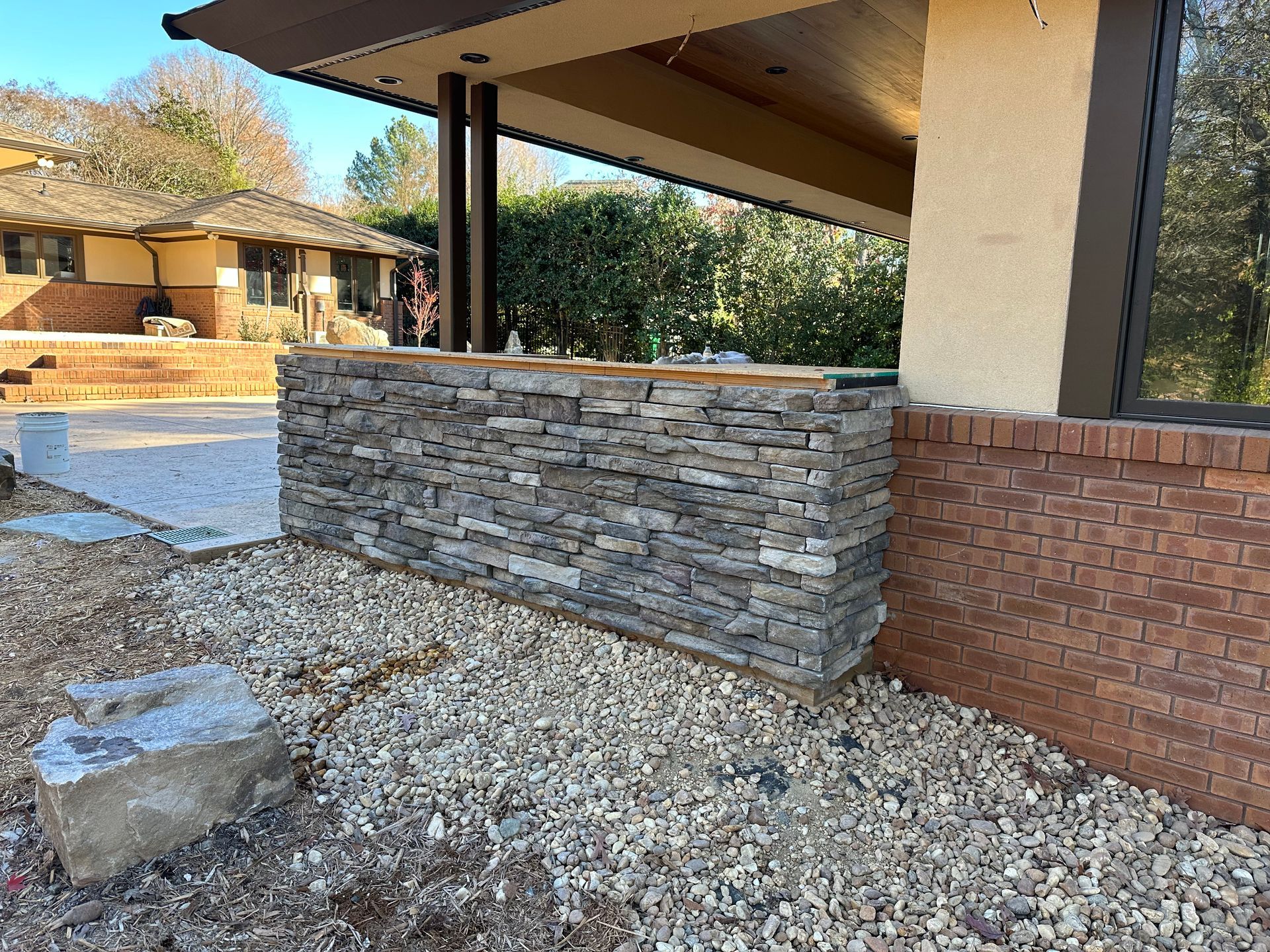 A stone wall is surrounded by gravel in front of a house.
