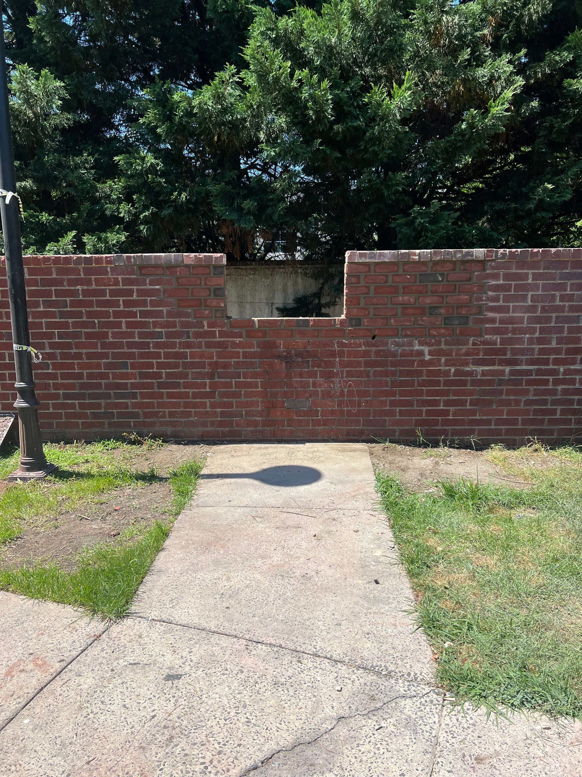 A brick wall with a hole in it is next to a sidewalk.