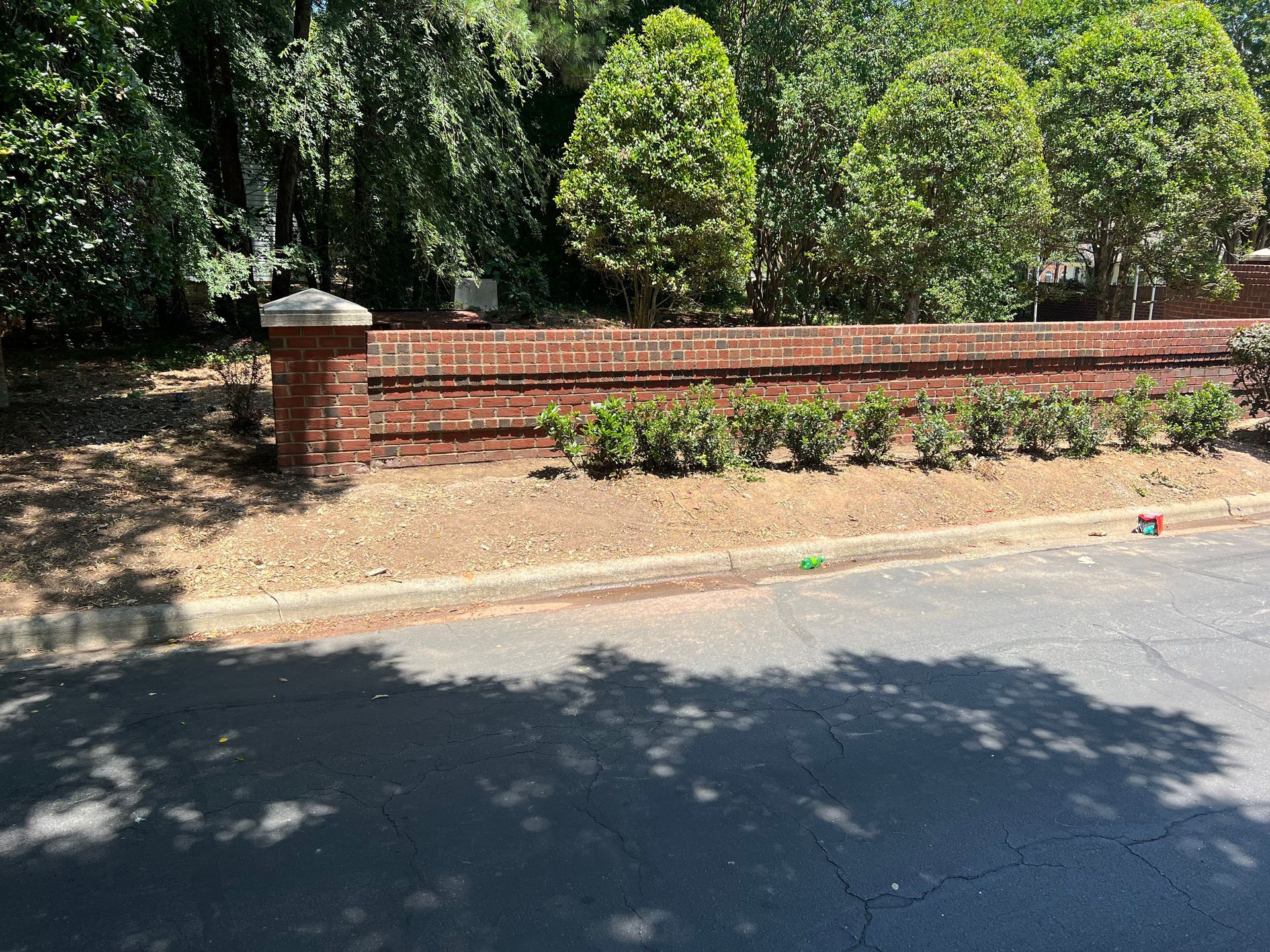 A brick wall surrounded by bushes and trees on the side of a road.