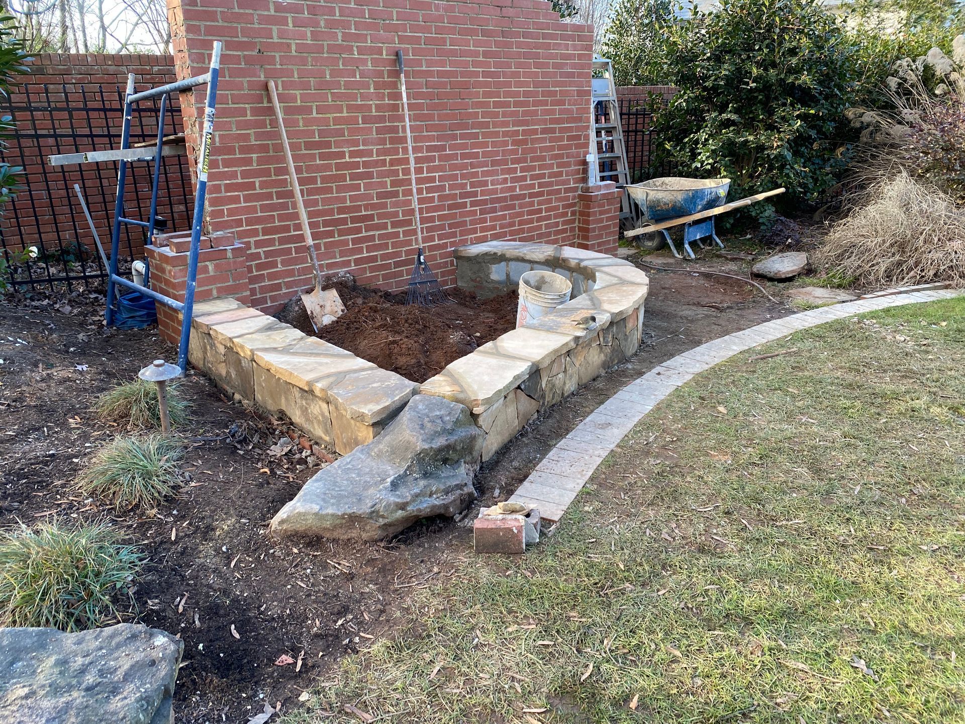 A stone wall is being built in a backyard next to a brick wall.