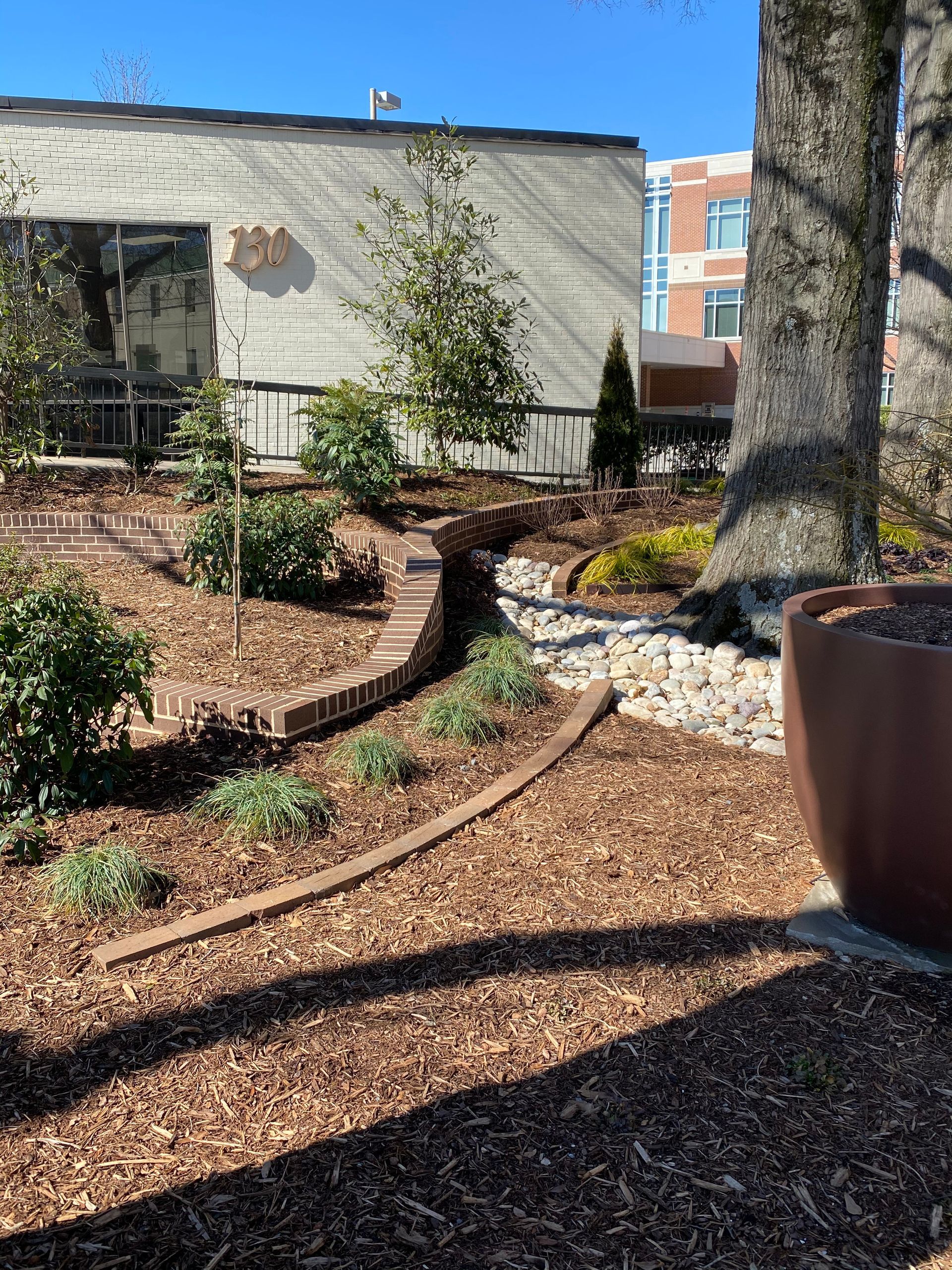 A garden with a brick building in the background and a tree in the foreground.