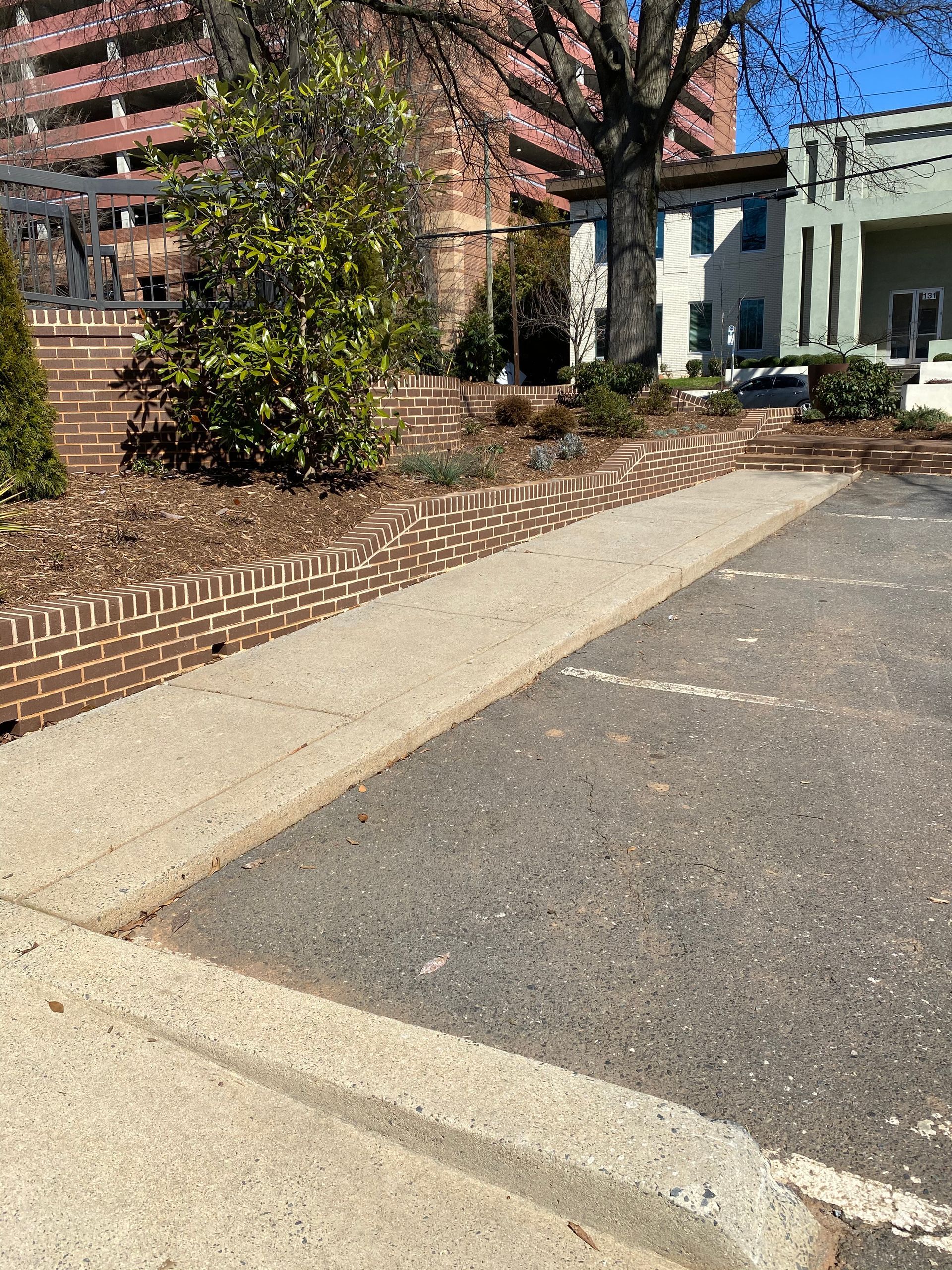 A sidewalk leading to a parking lot with a brick wall in the background.