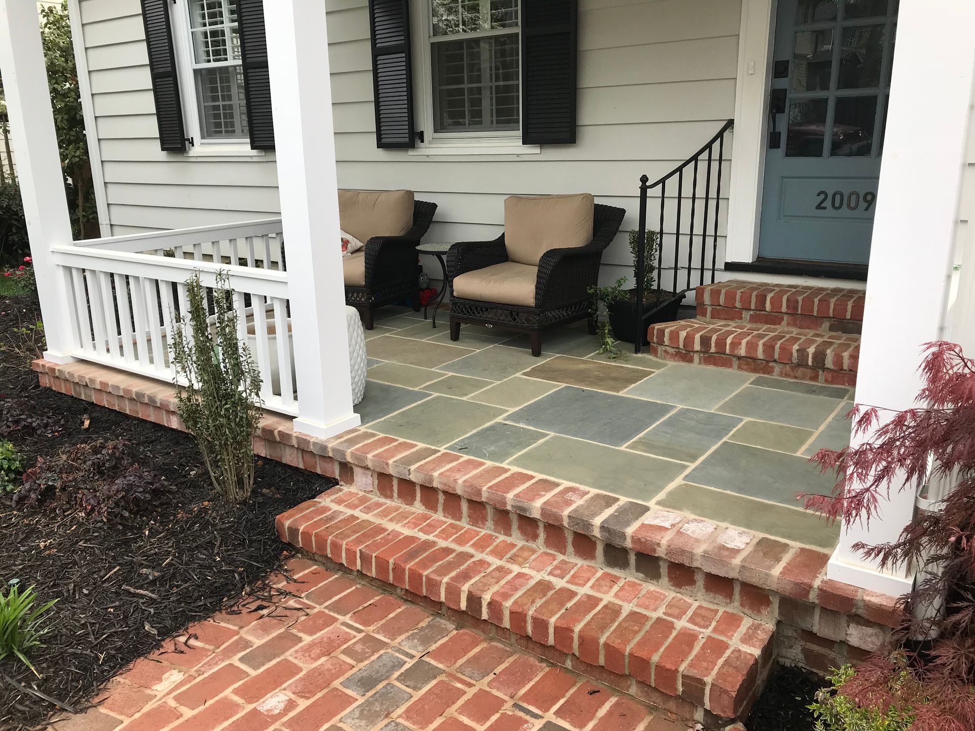 A porch with a brick walkway and chairs on it