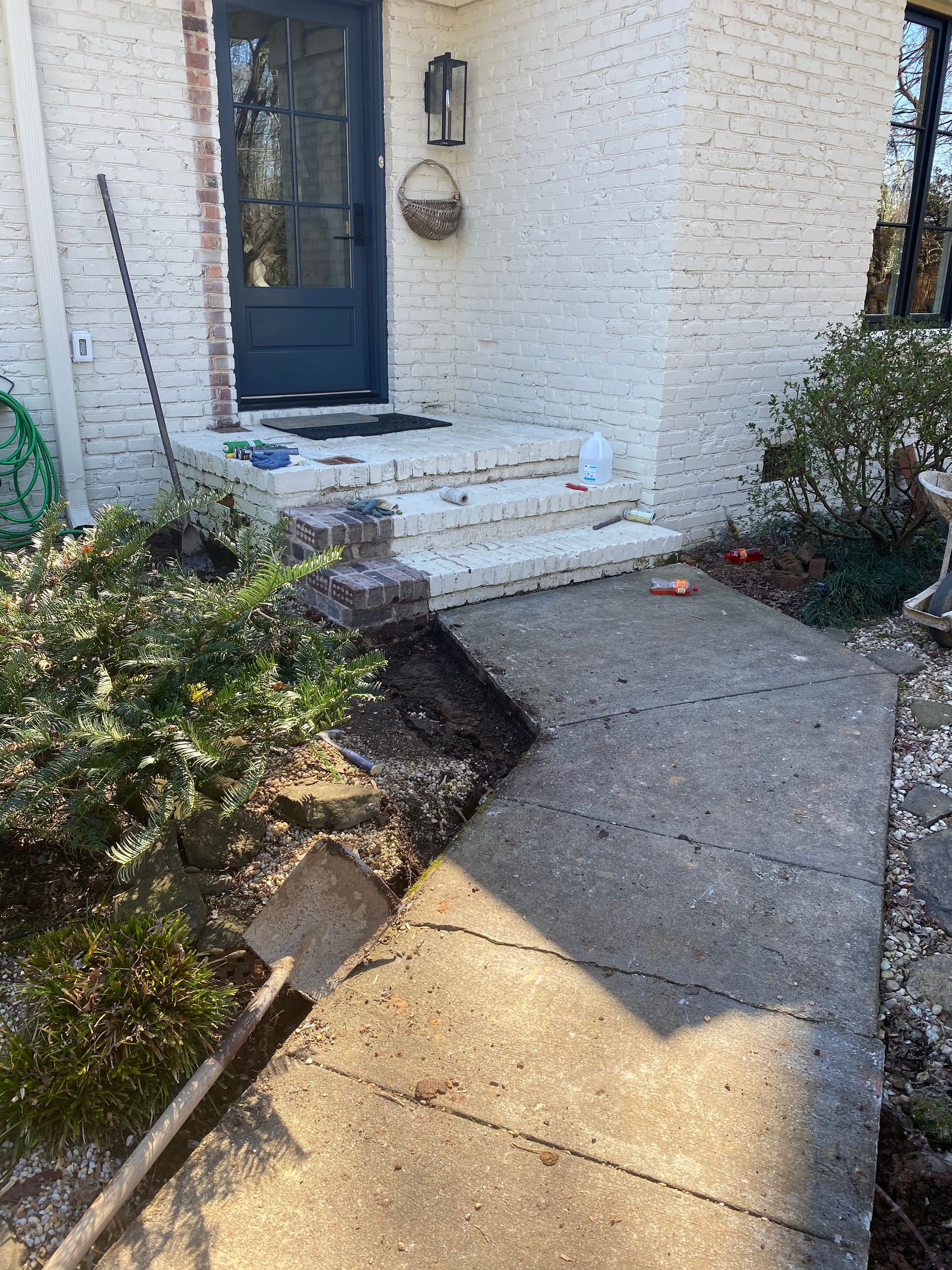 A shovel is sitting on the sidewalk in front of a white brick house.