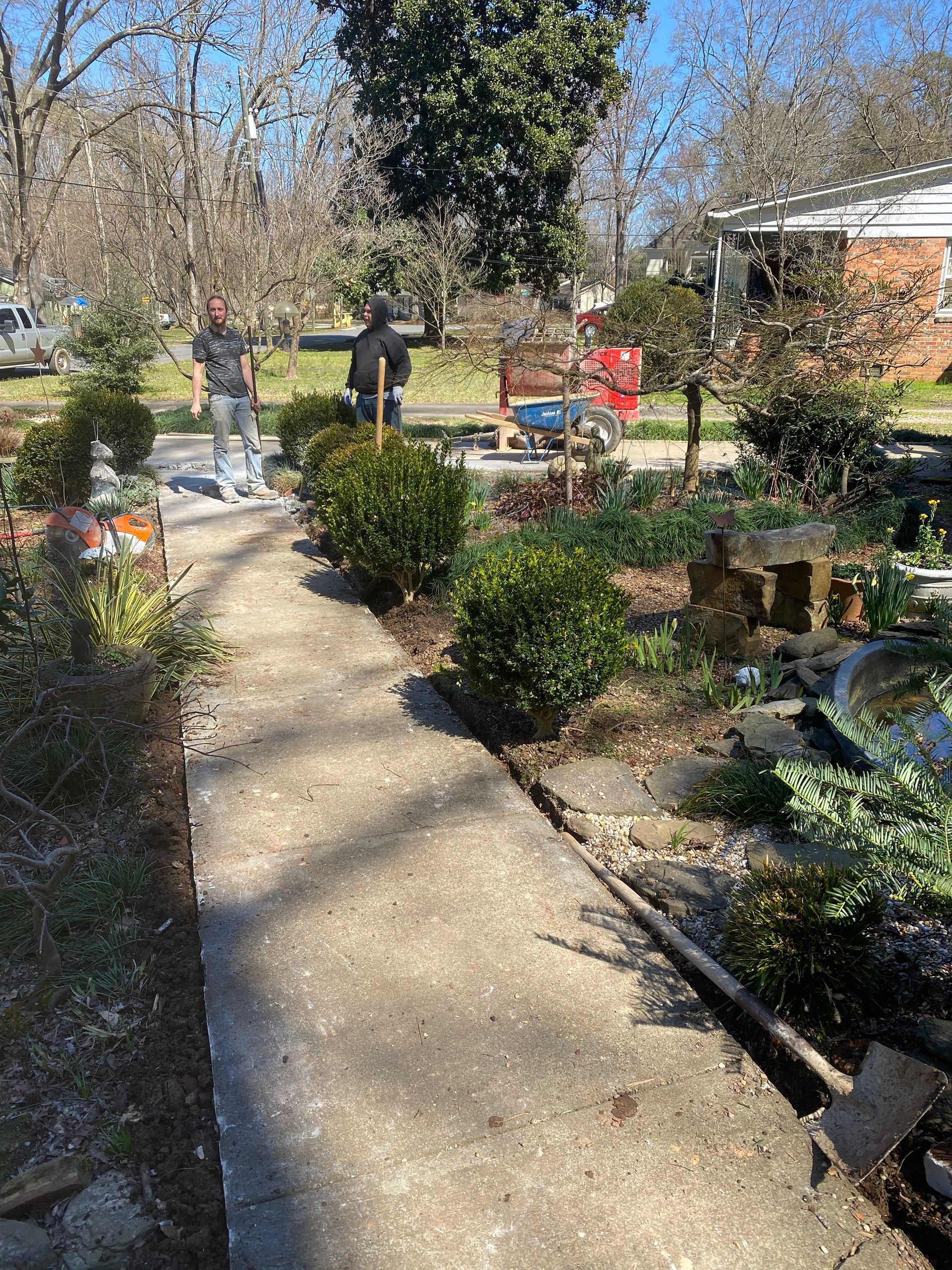 A concrete walkway leading to a garden with trees and bushes.