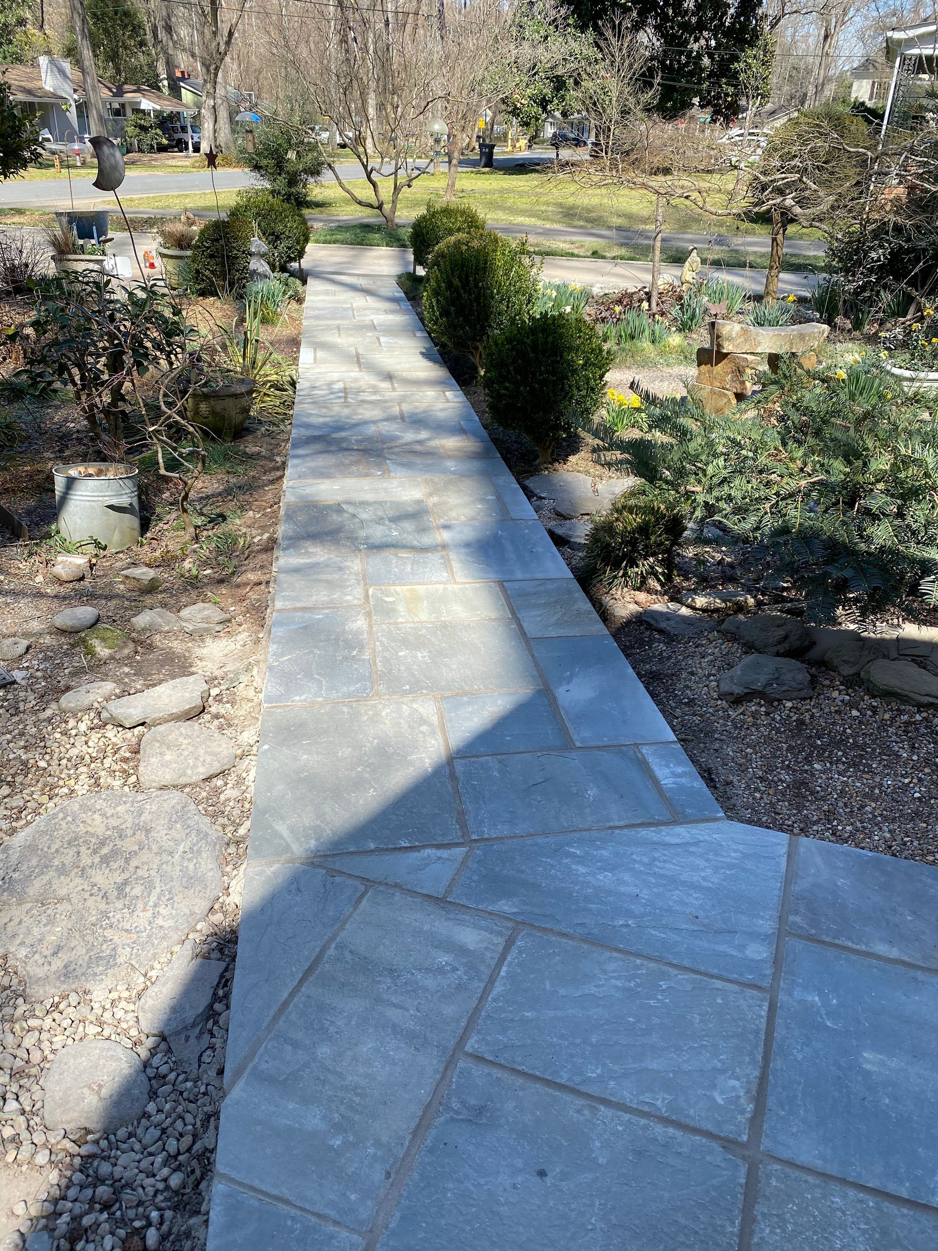 A stone walkway leading to a garden with trees and bushes.