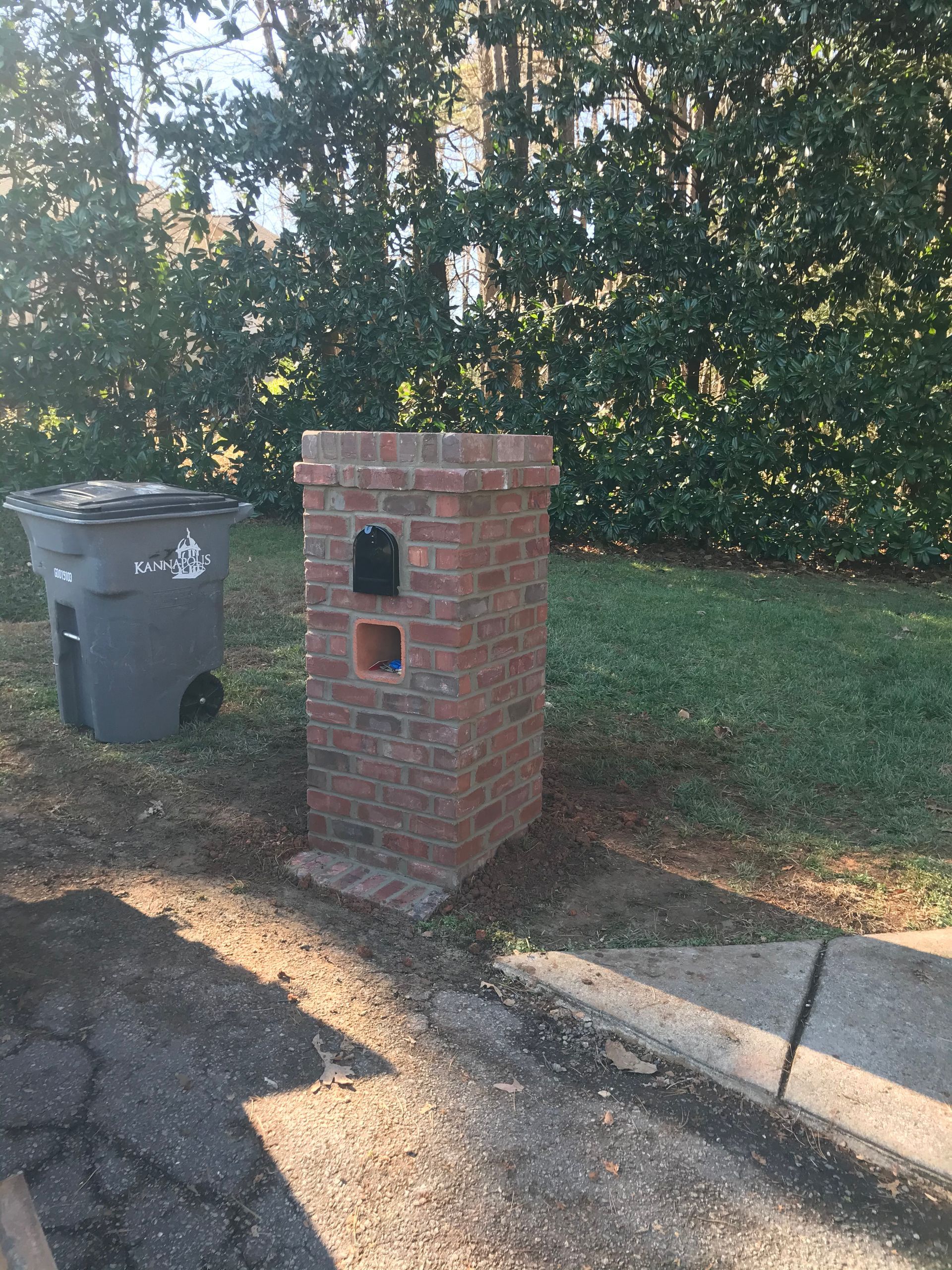 A brick chimney is sitting next to a trash can in a yard.