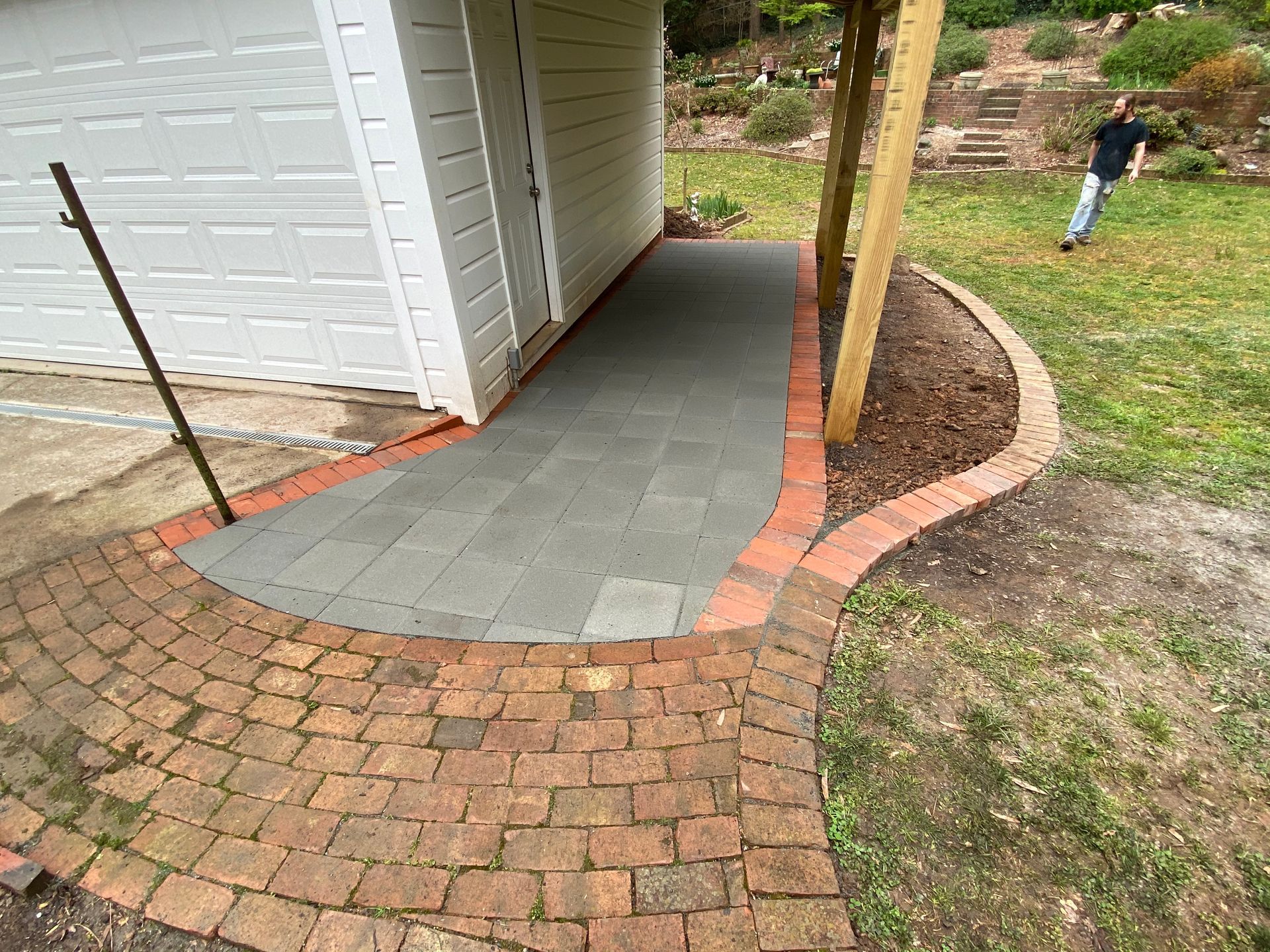 A man is standing next to a brick walkway leading to a garage.