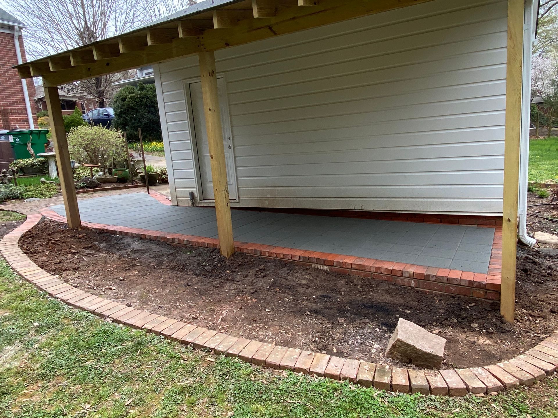 A white shed with a wooden roof and a brick border in front of it.