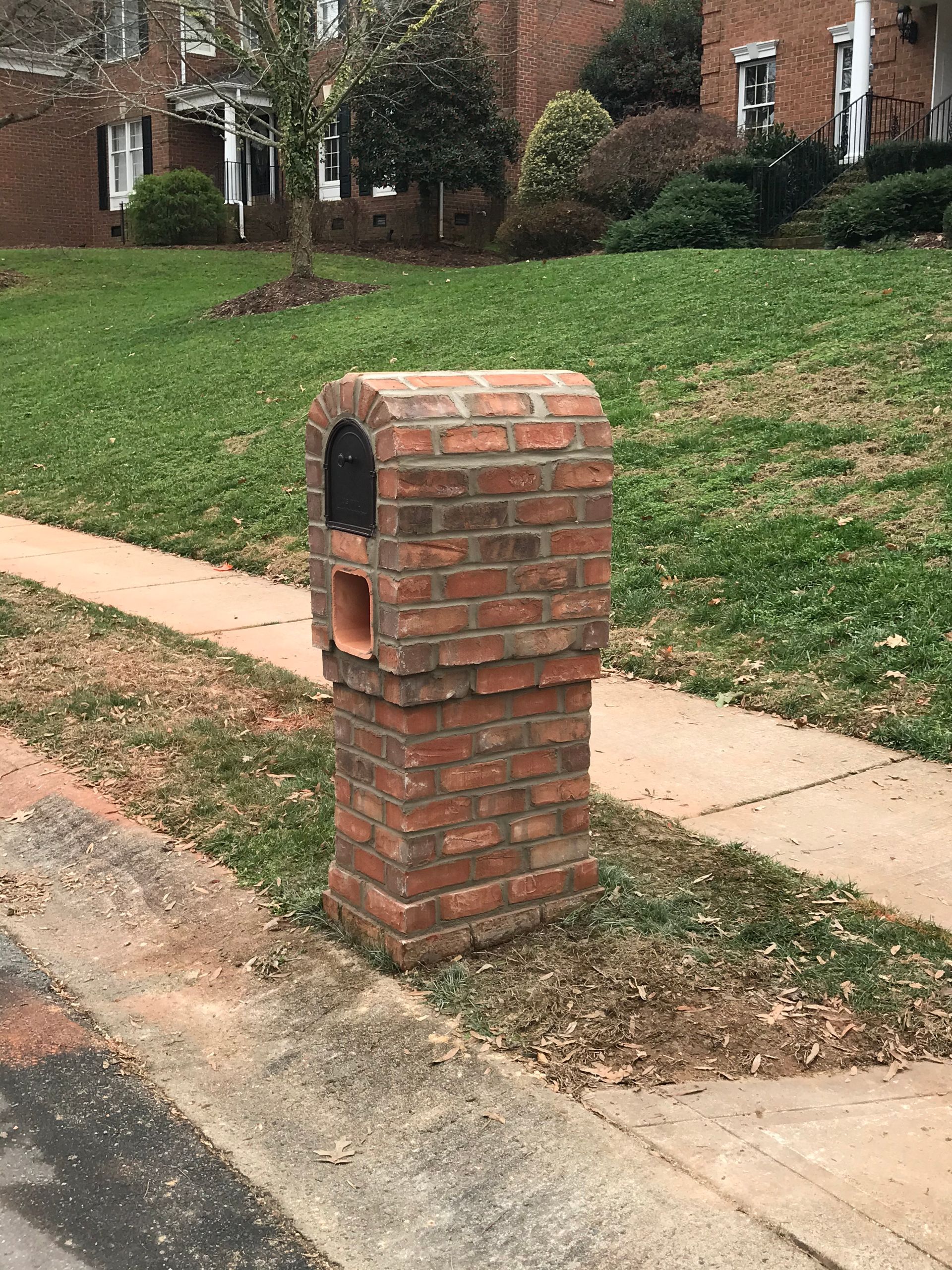 A brick mailbox is sitting on the side of the road next to a sidewalk.