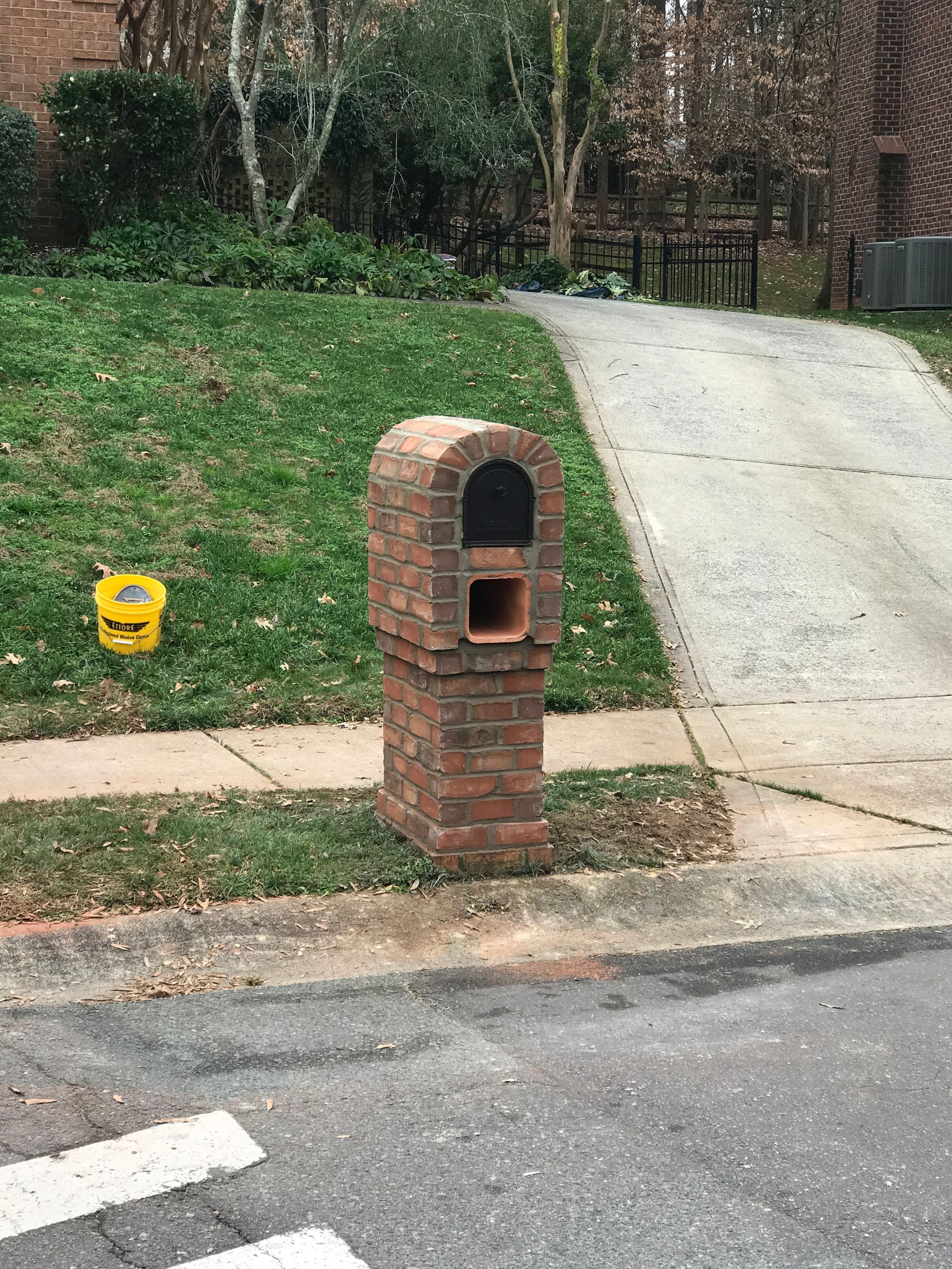 A brick mailbox is sitting on the side of the road next to a sidewalk.