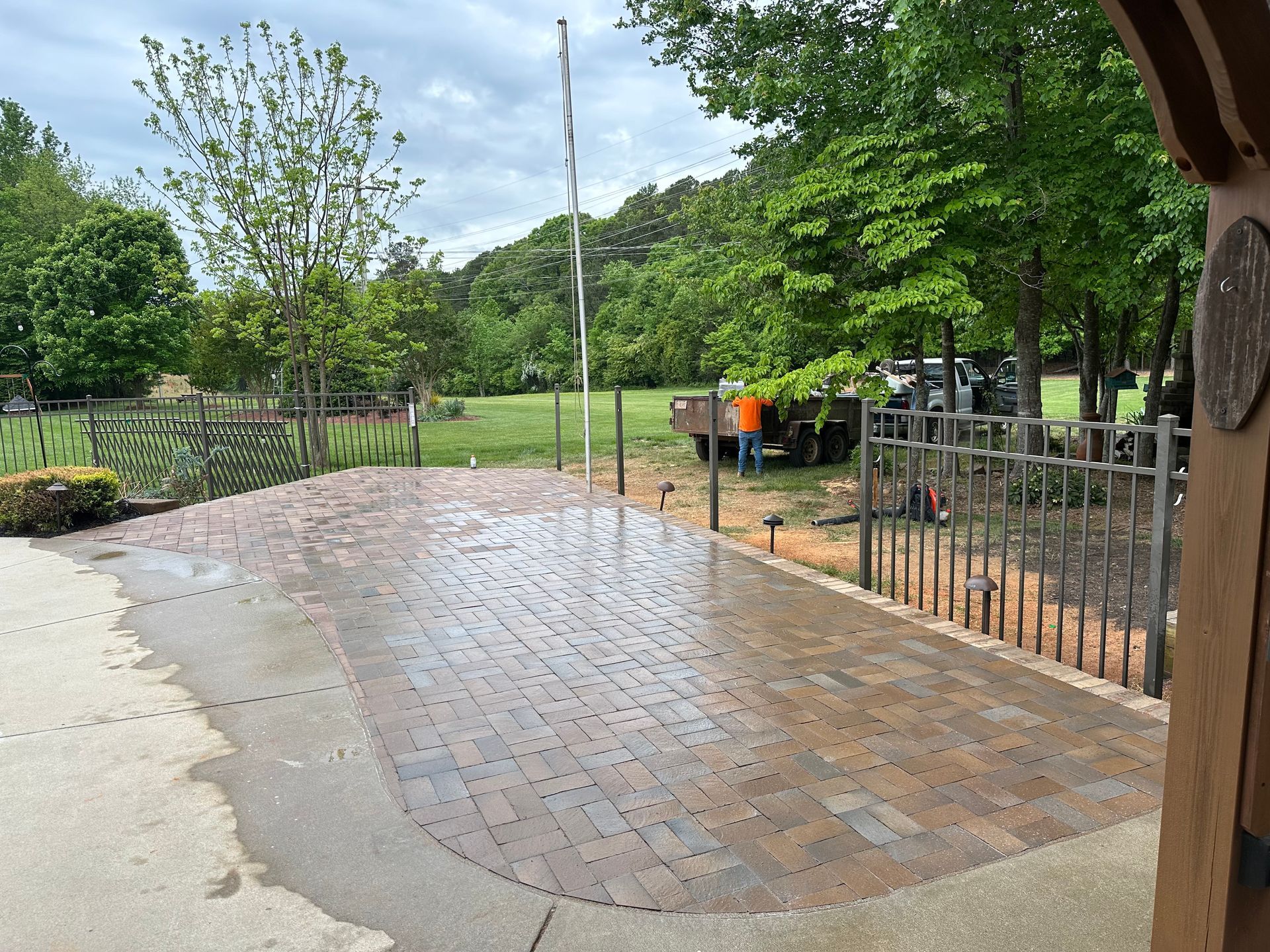 A brick driveway with a fence and trees in the background.