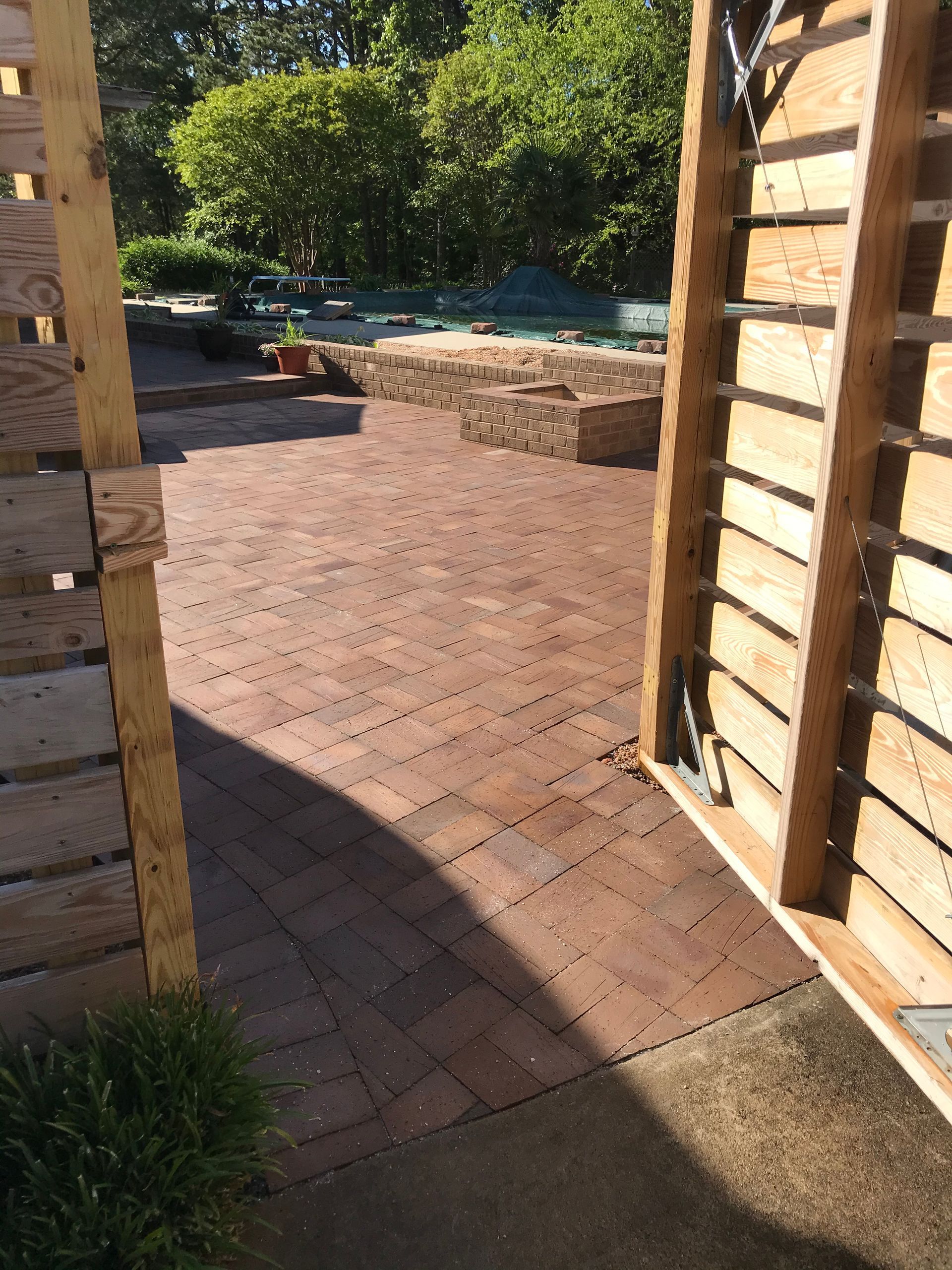 A wooden fence is surrounding a brick patio with a pool in the background.
