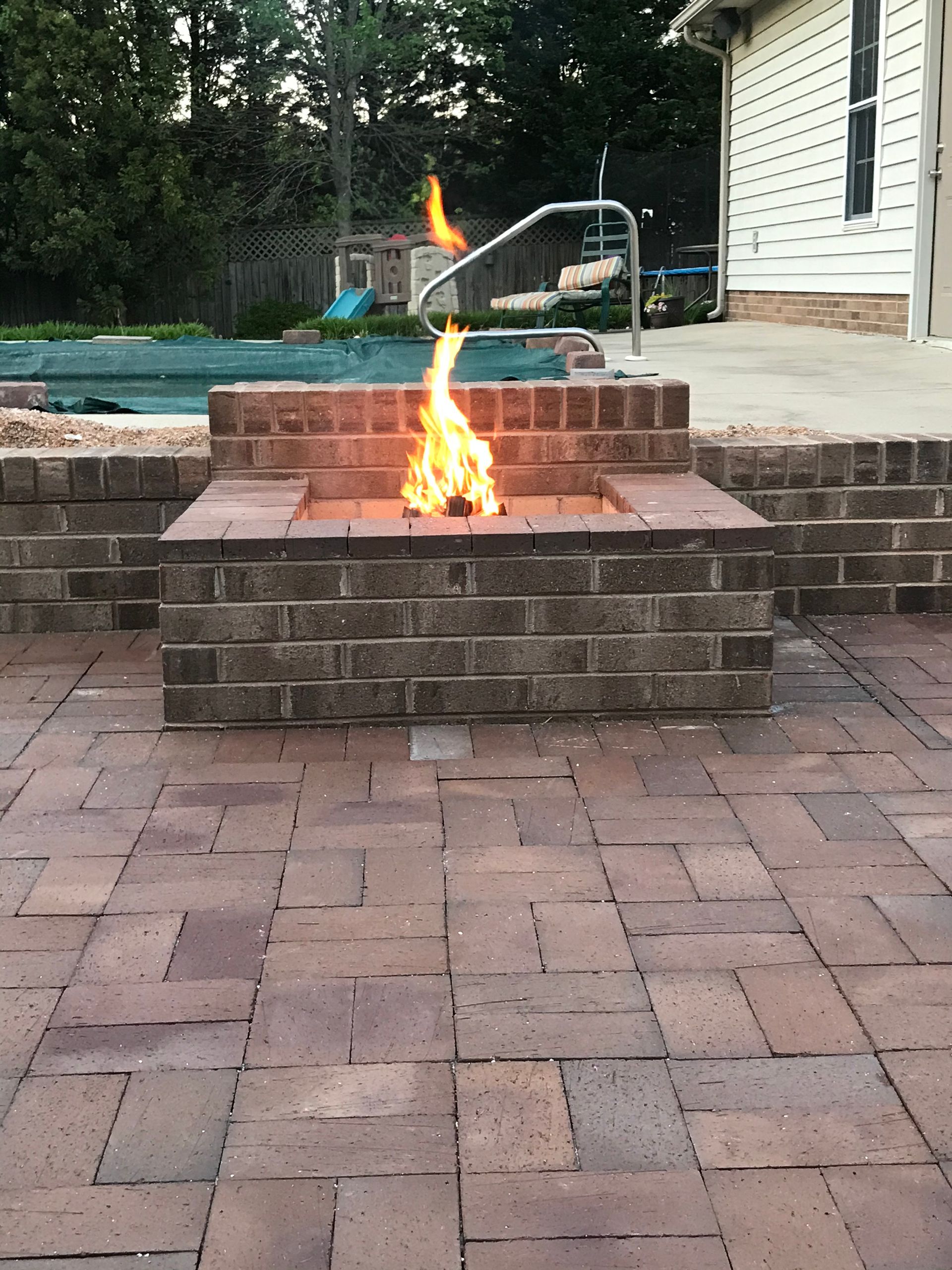 A fire pit is sitting on a brick patio next to a pool.
