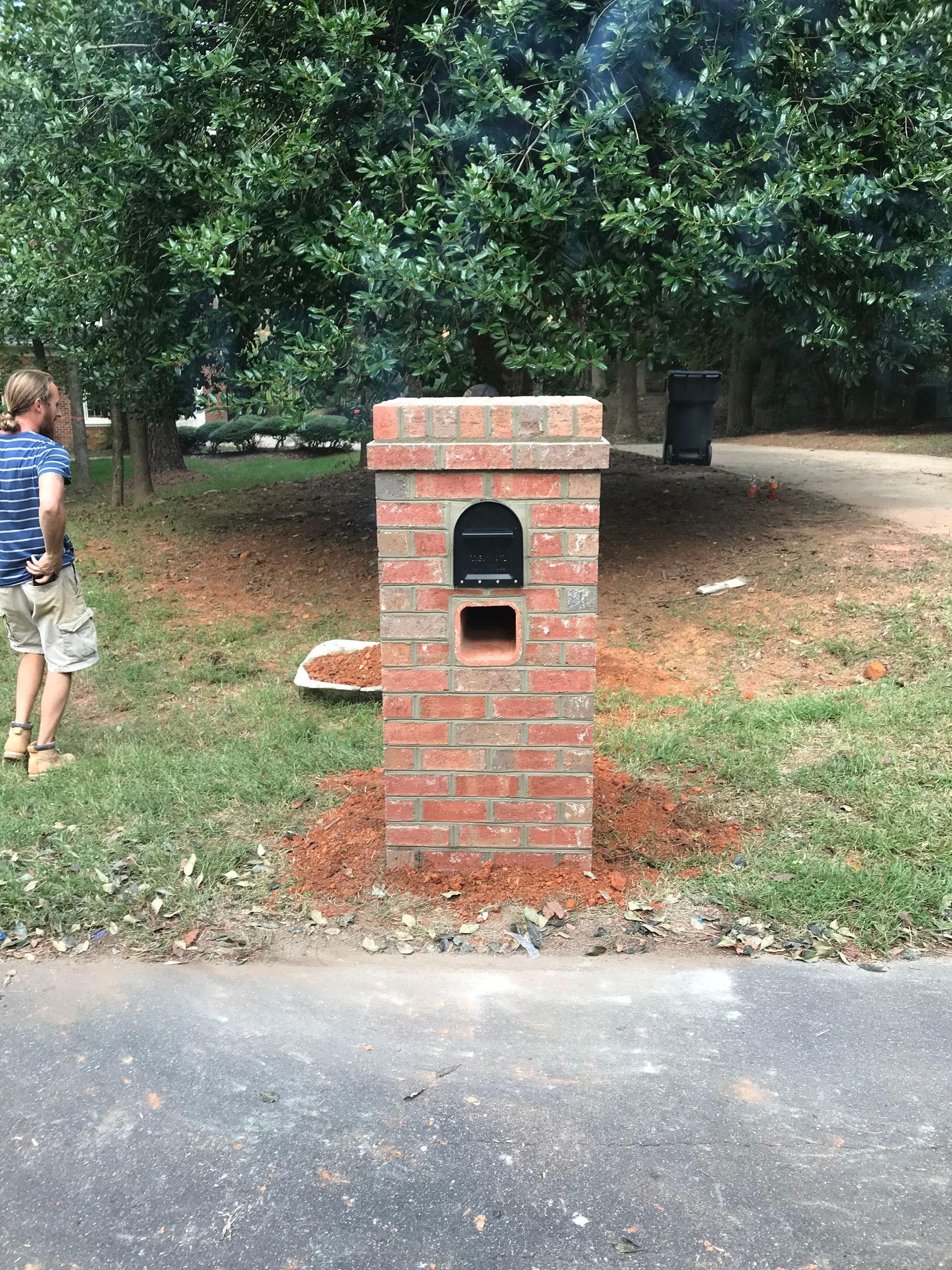 A man is standing next to a brick mailbox in the grass.