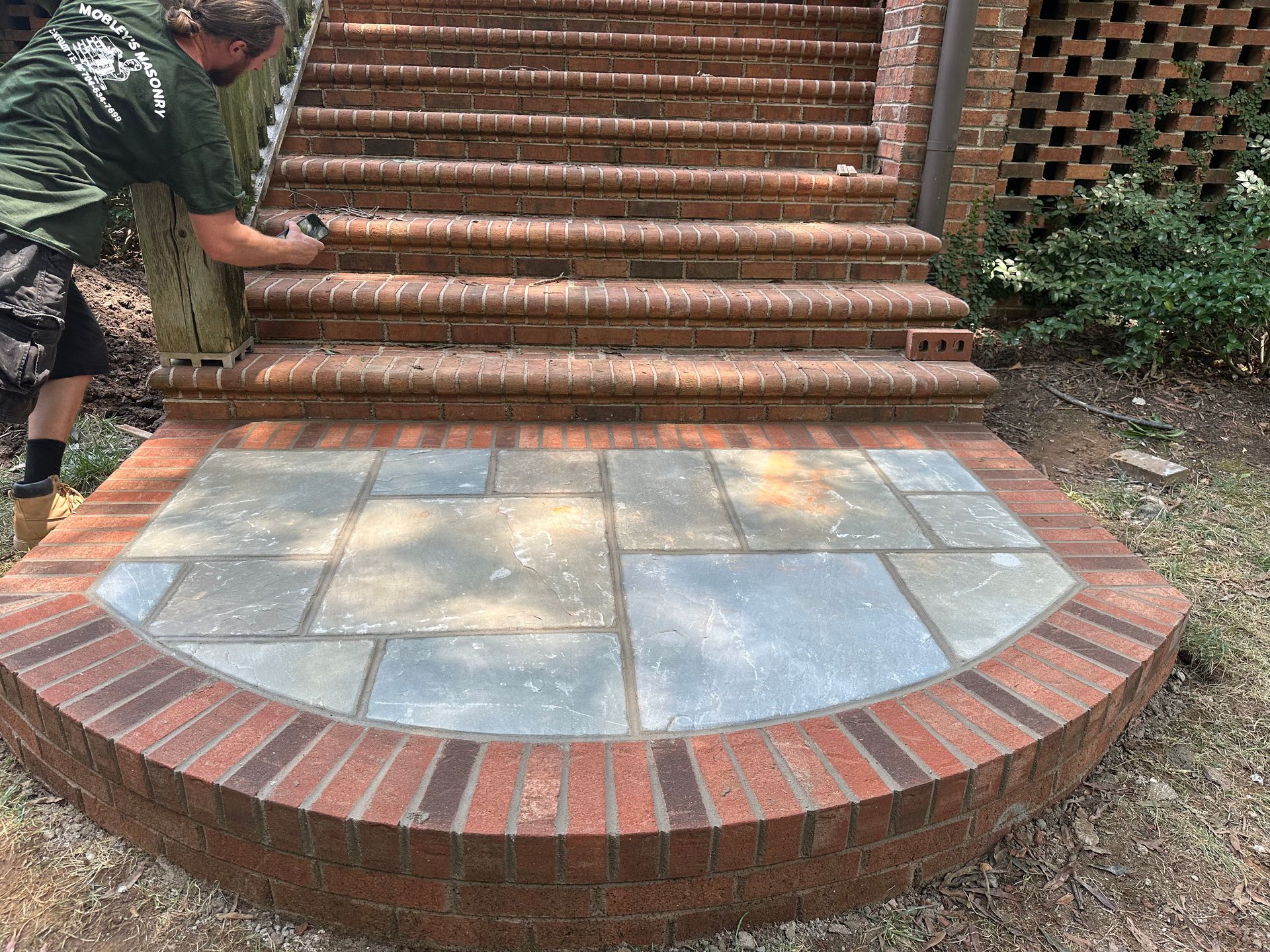 A man is working on a brick walkway next to a set of stairs.
