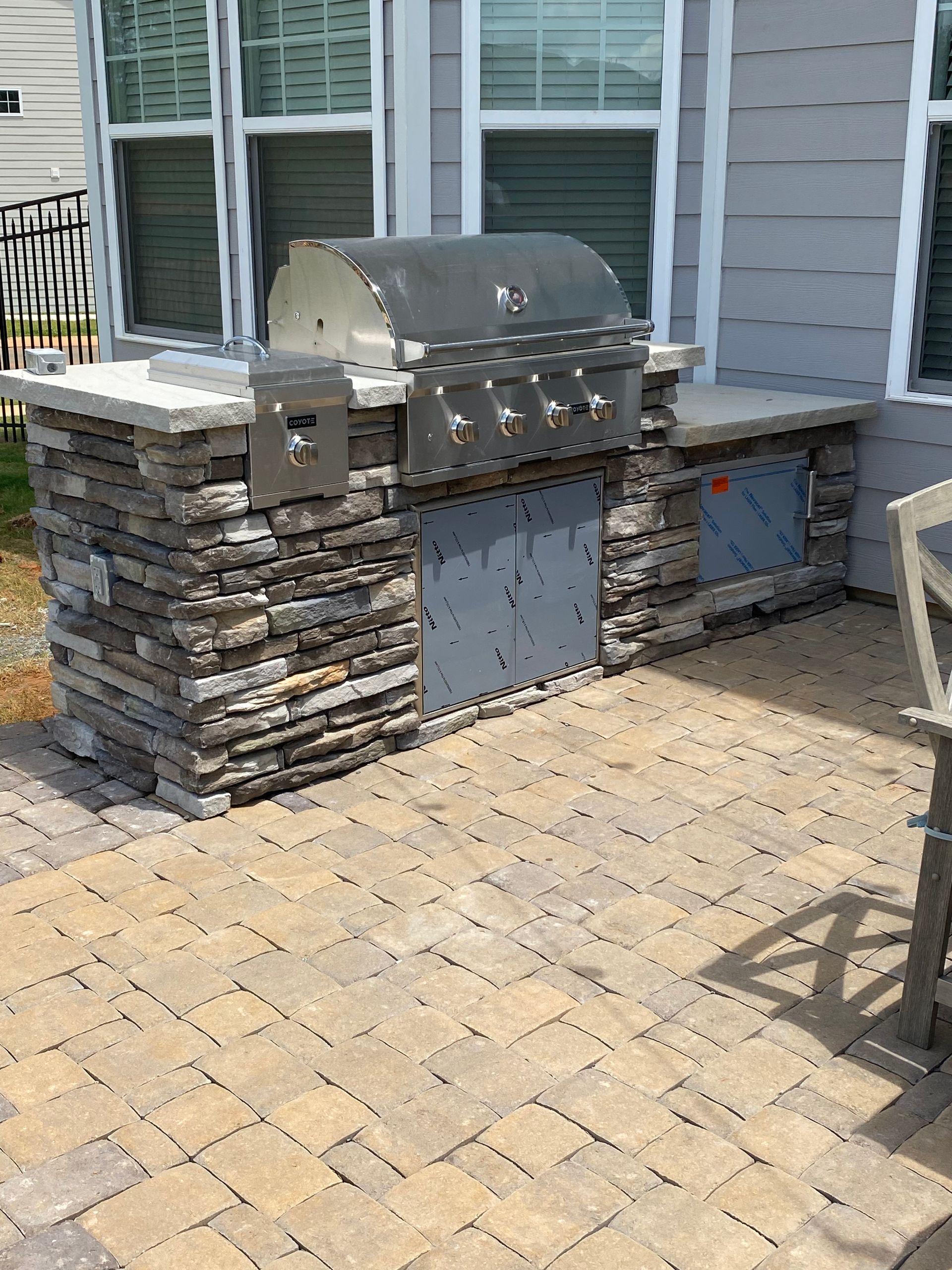 A grill is sitting on a brick patio in front of a house.