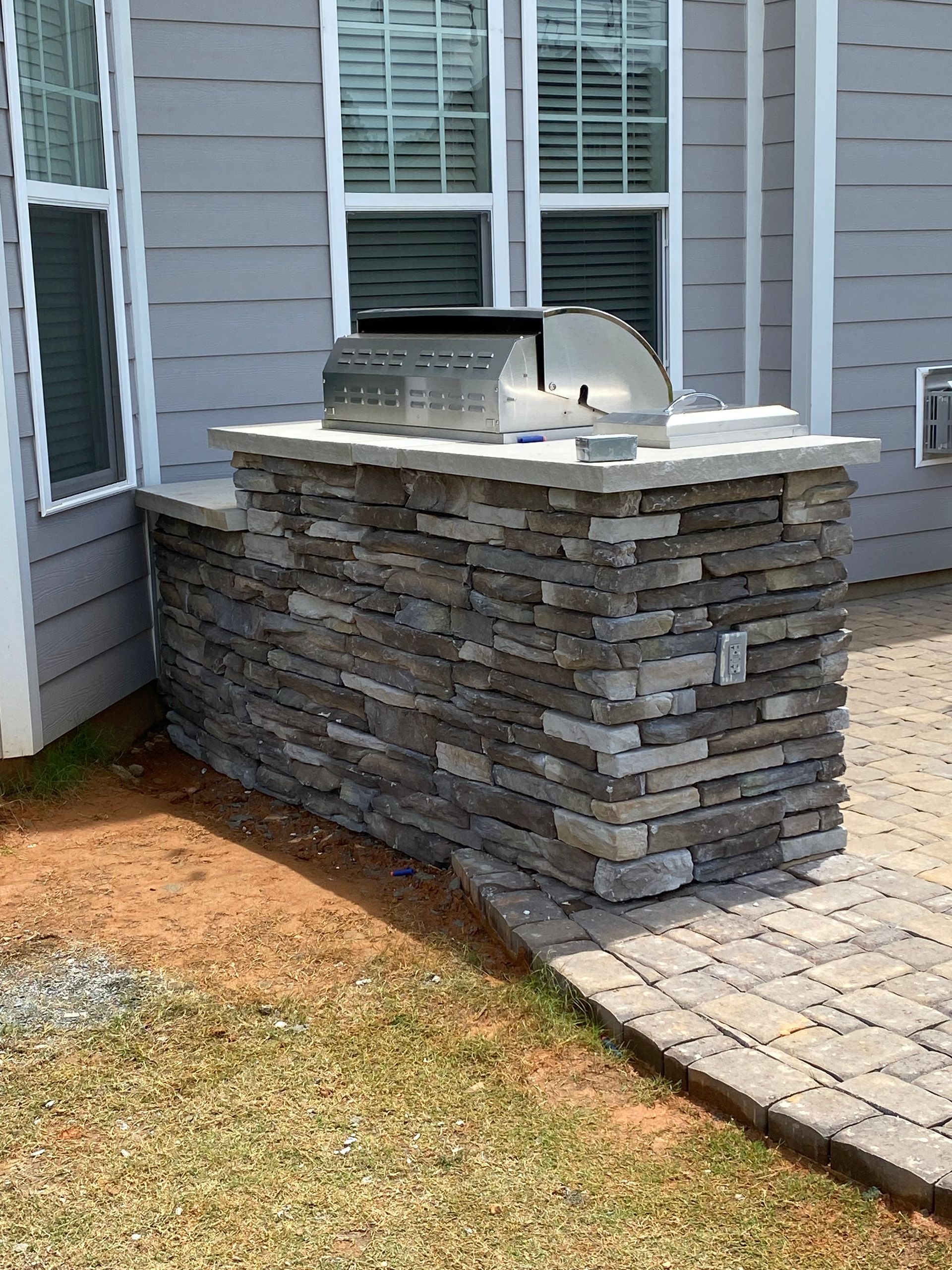 A brick wall with a grill on top of it in front of a house.