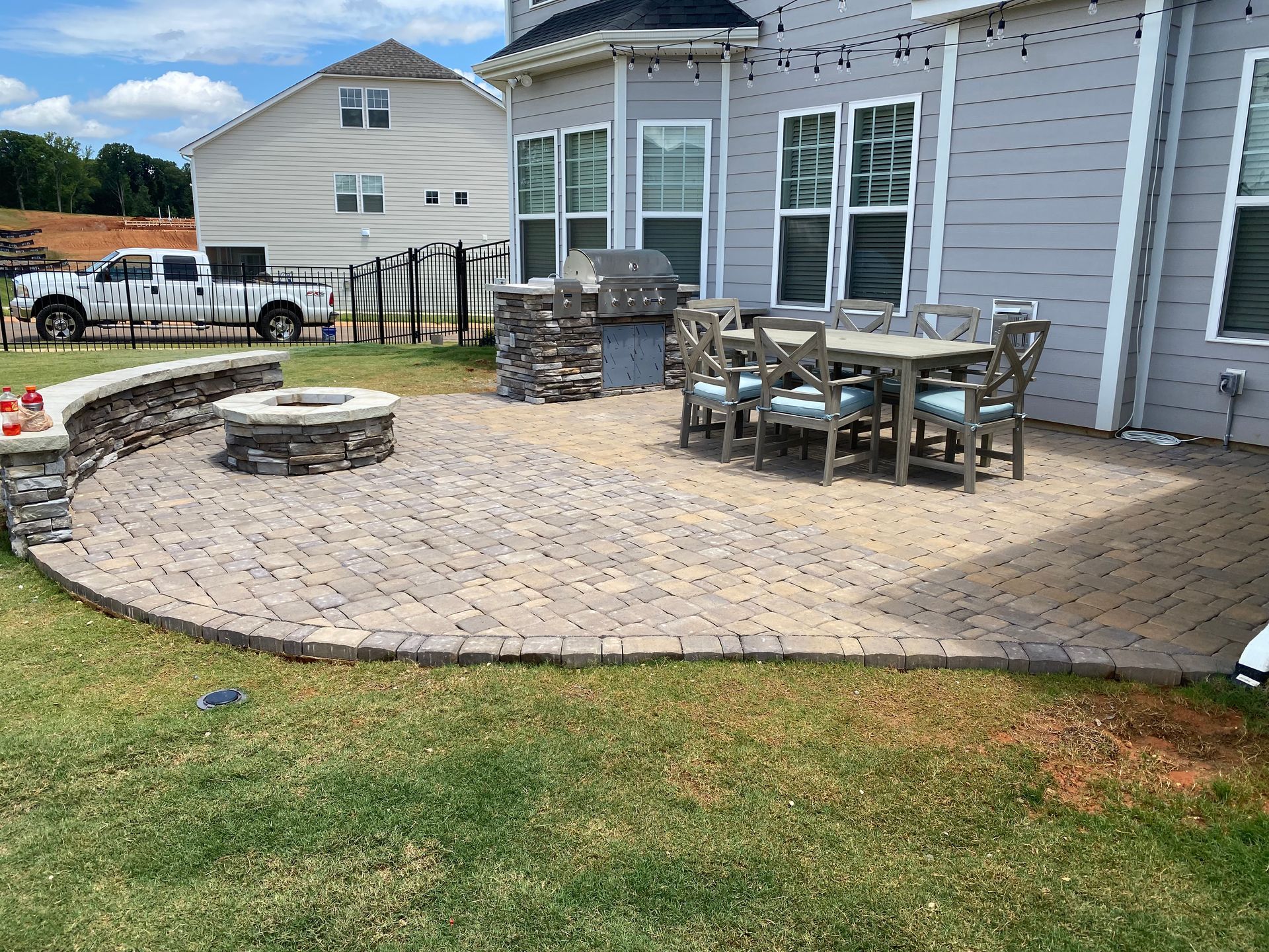 A patio with a fire pit , table and chairs in front of a house.