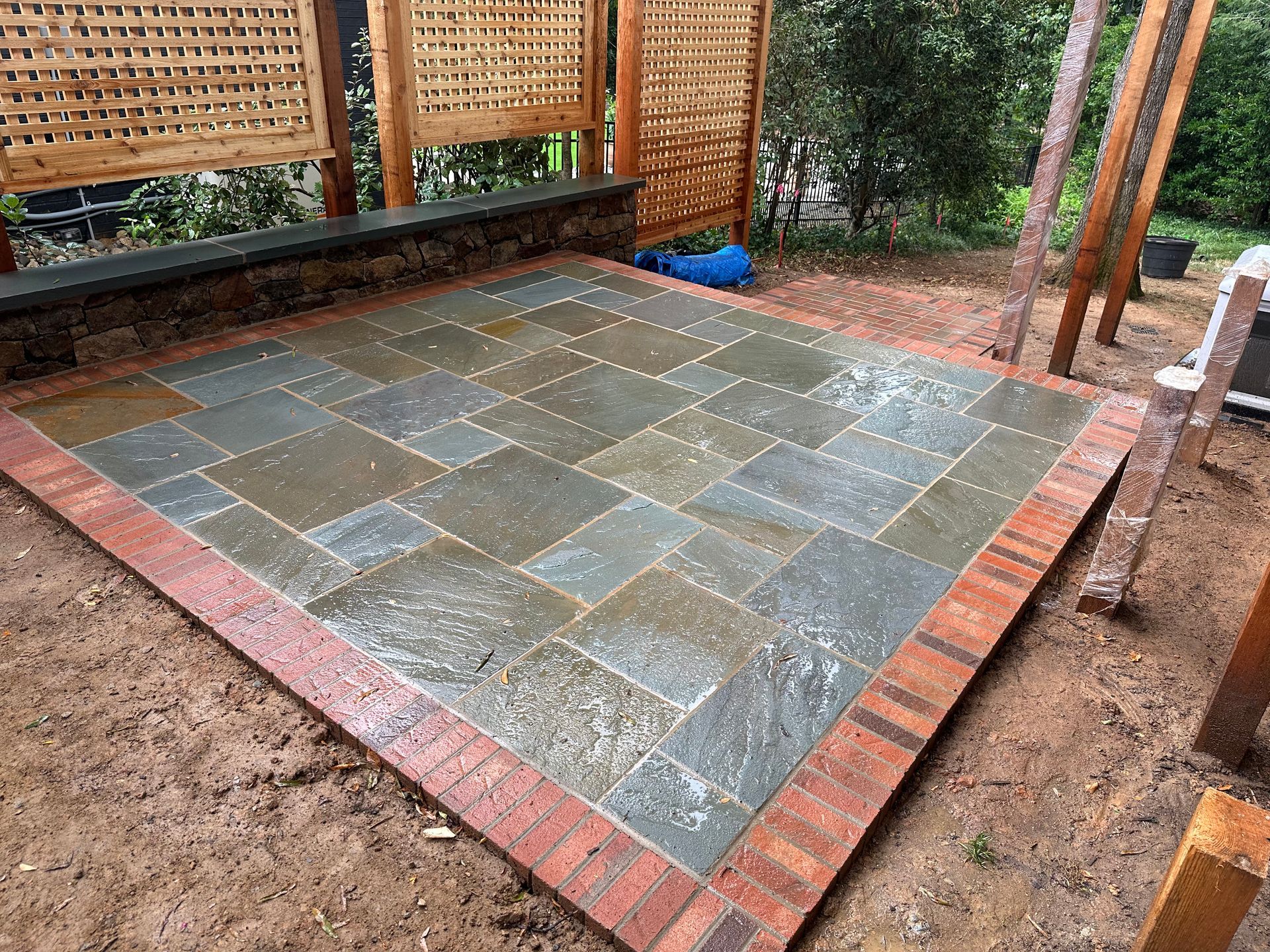 A stone patio with a brick border is being built in a backyard.