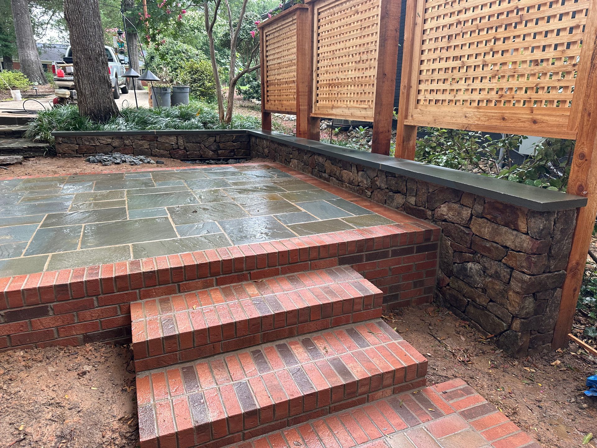 A brick patio with stairs leading up to it and a wooden fence.