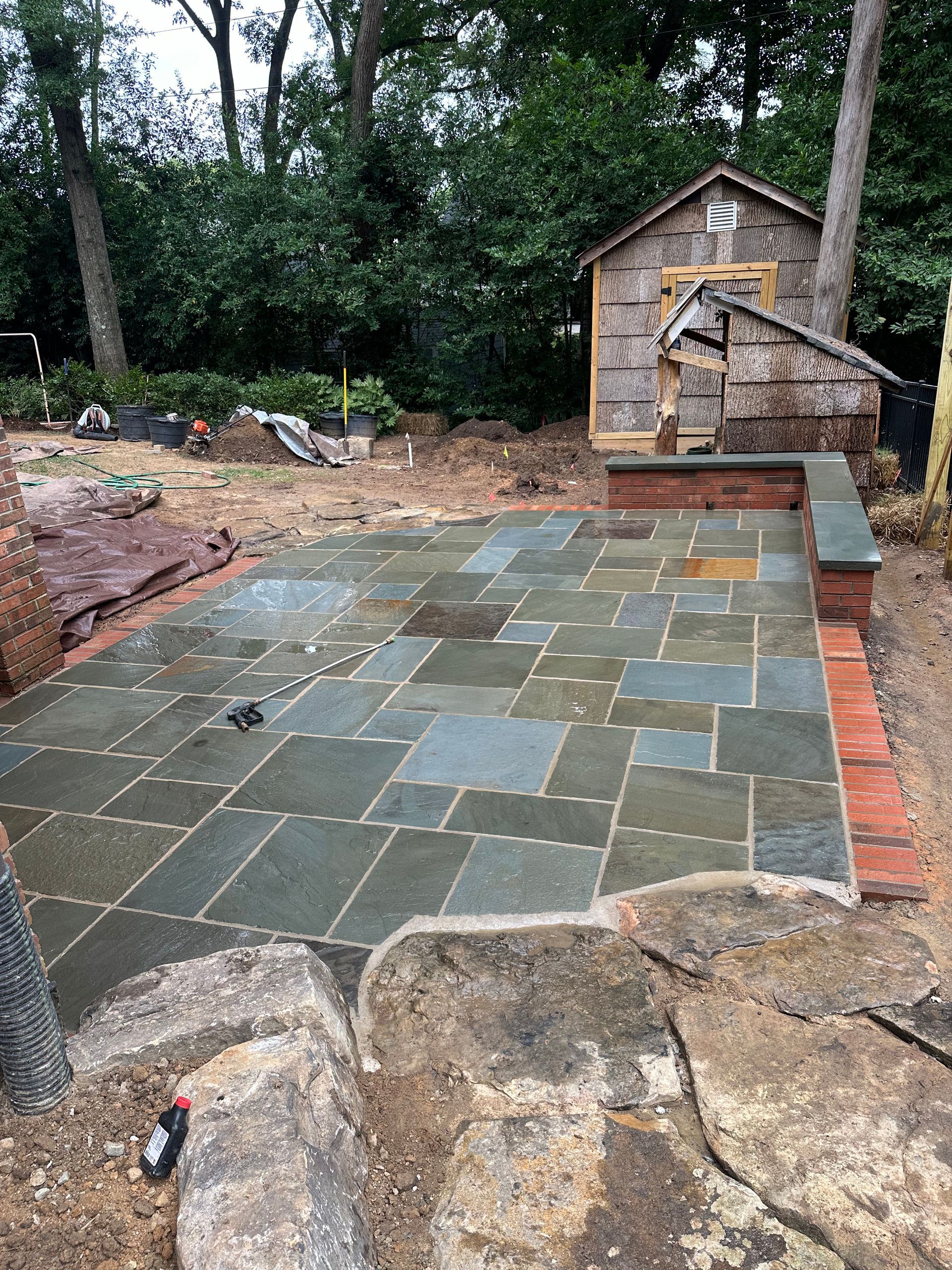 A patio is being built in a backyard with a shed in the background.