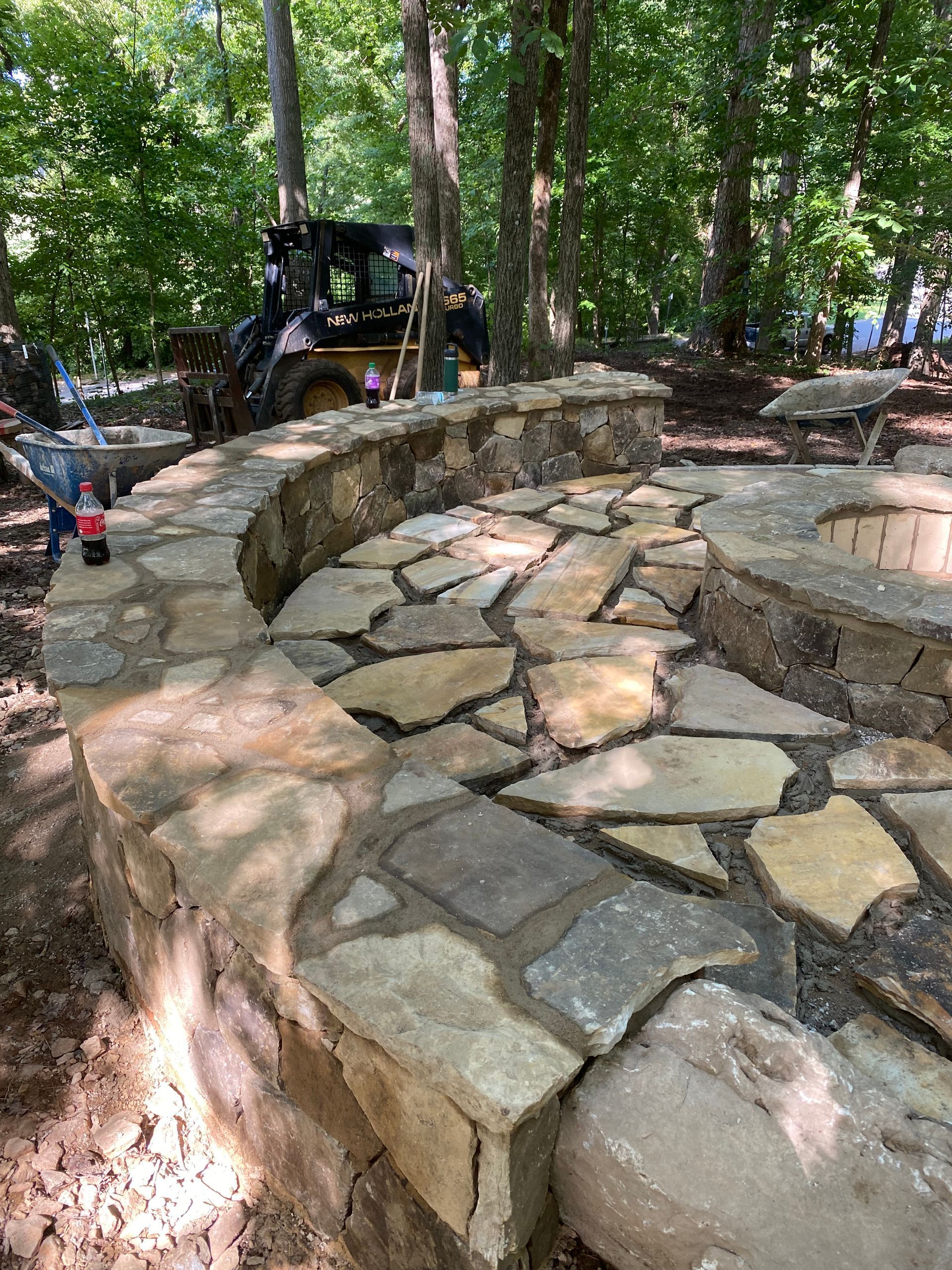 A stone wall is being built around a fire pit in the woods.