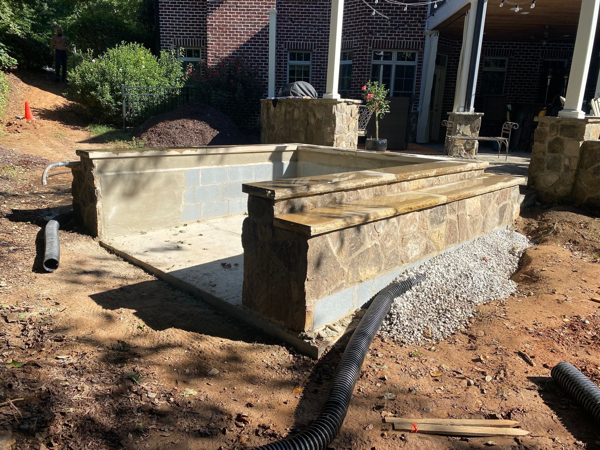 A large stone wall is being built in front of a brick house.