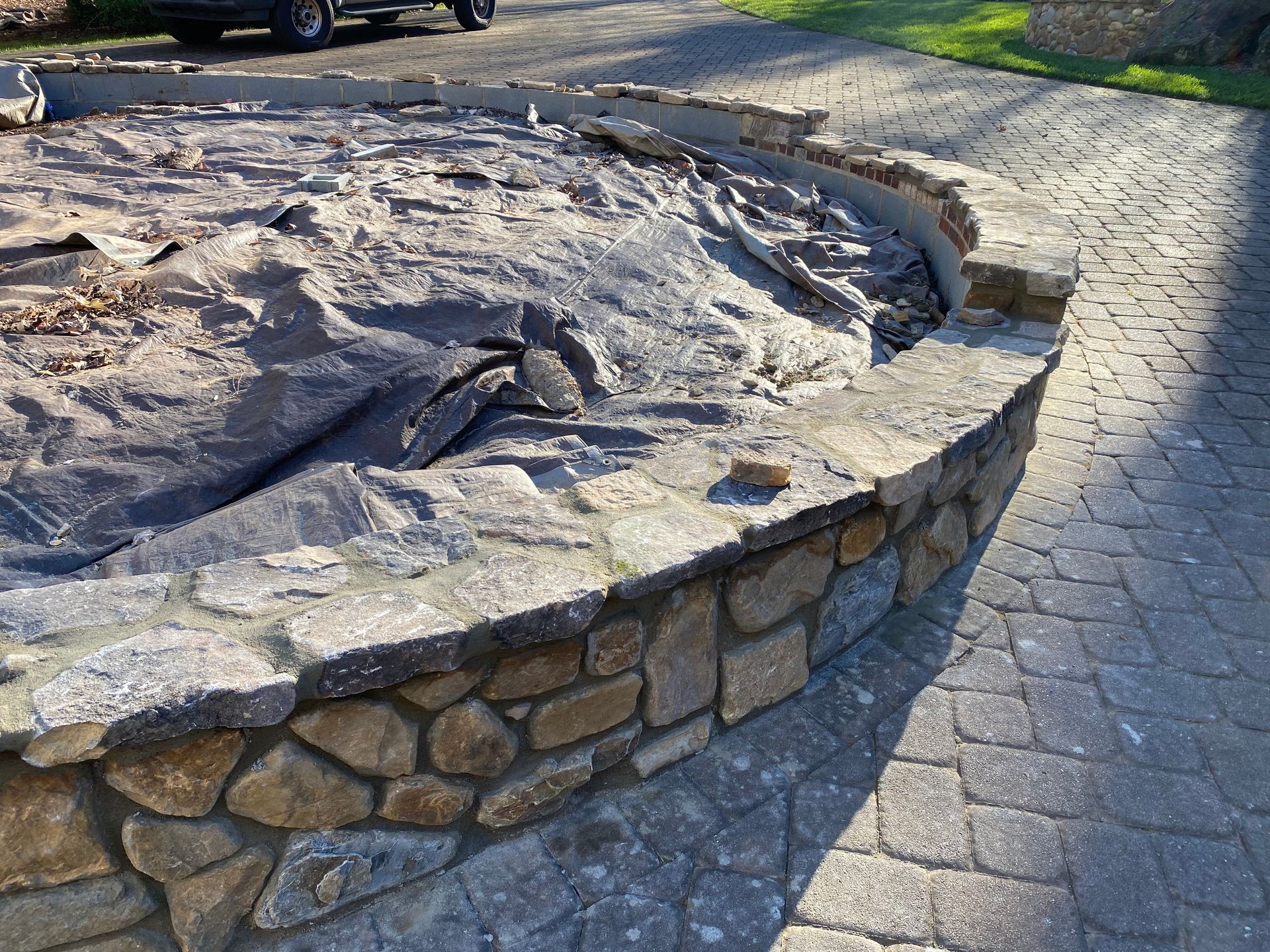 A stone wall with a tarp on top of it and a car parked in the background.