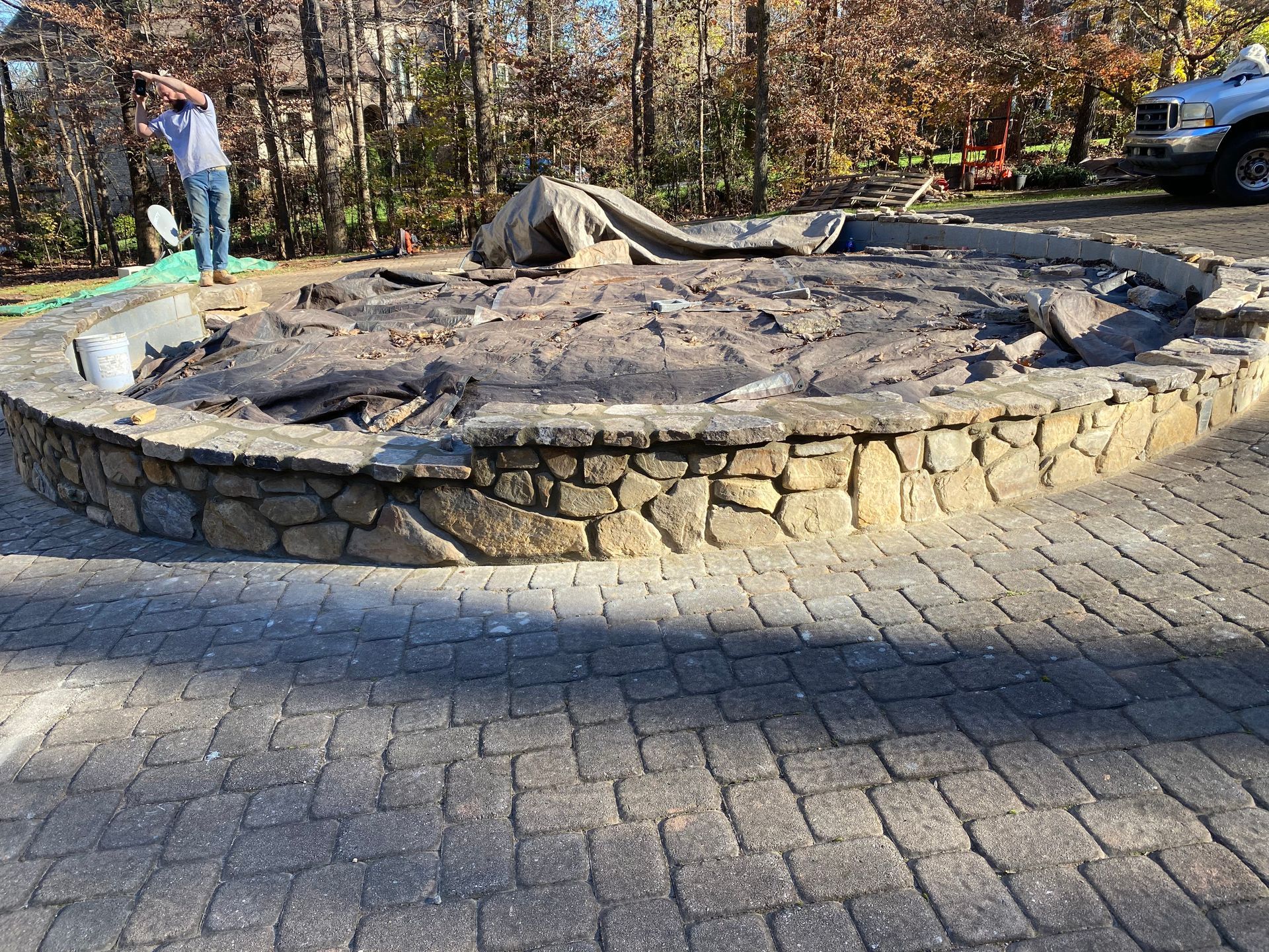 A man is working on a stone wall in a driveway.